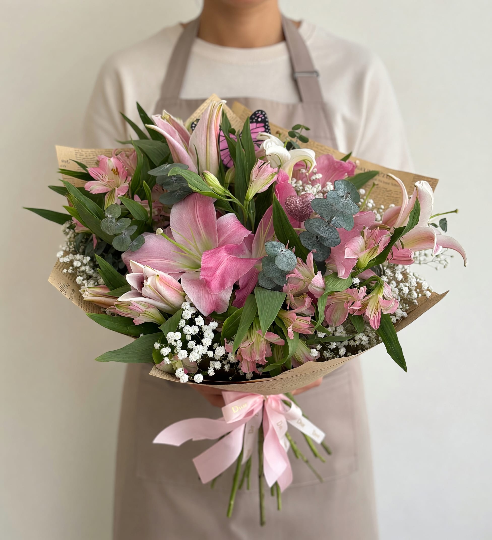 Chic Lilies &amp; Alstroemeria Mix Bouquet Freestyle  - Large pink and white lilies mingle with delicate pink alstroemeria and cloud-like clusters of white filler flowers in this Chic Lilies Mix bouquet-an airy, hand-tied flower arrangement perfect for birthdays, Mother's Day, anniversaries, or a thoughtful everyday gift. The pastel palette reads romantic and fresh, so the person you're thinking of will feel gently celebrated the moment they see the soft pink blooms contrasted with crisp white accents and deep green foliage.  Wrapped in brown or printed paper and finished with a pale pink satin ribbon, this bouquet has a relaxed, gift-ready presentation that feels both personal and polished. Eucalyptus-like round foliage adds a cool green-gray contrast and texture, while the layered mix of large lilies and smaller alstroemeria creates a full, tactile look that stays visually interesting from every angle. Care: keep stems in fresh water, recut stems before arranging, and display away from direct heat to extend vase life.