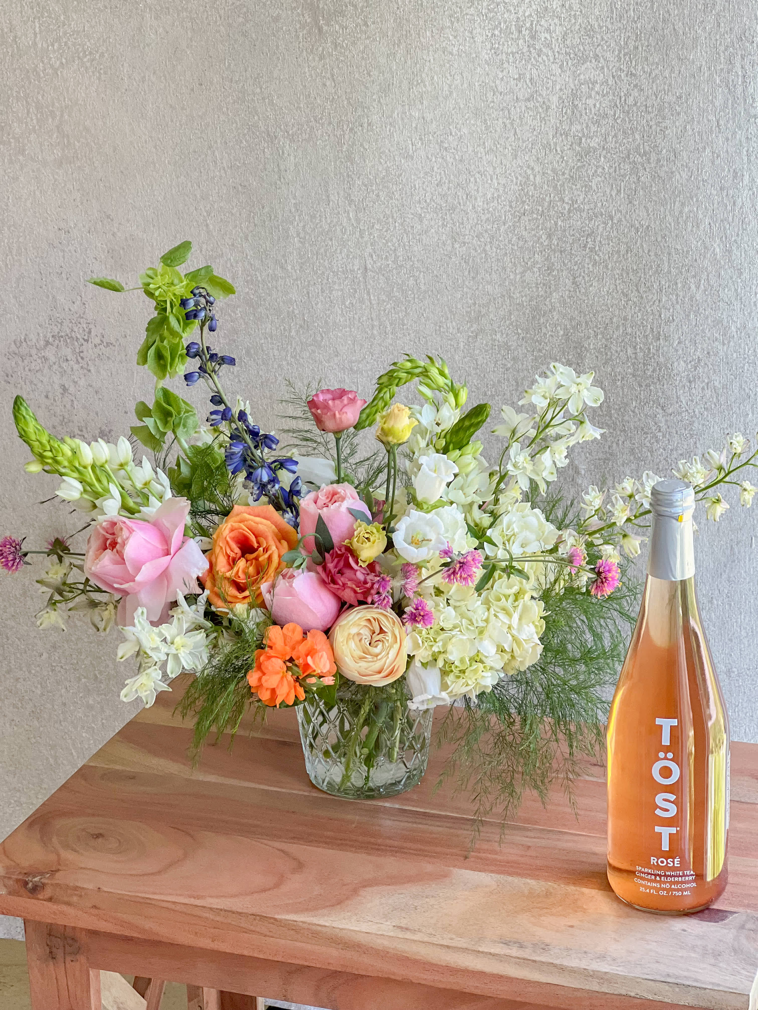 Mixed bouquet in a glass vase beside a bottle of rosé sparkling drink