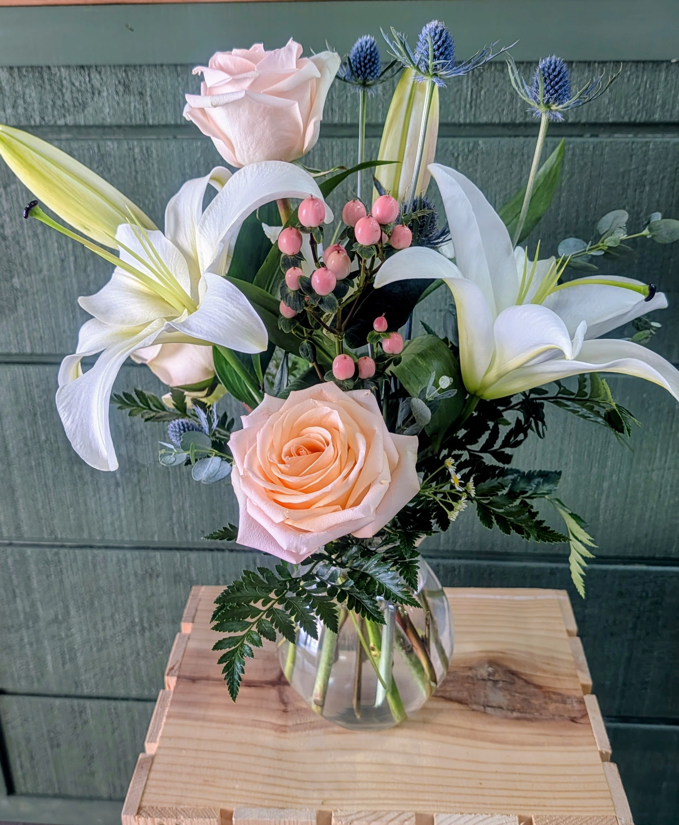 Love w/ Lilies - Pale pink roses and large white lilies form a soft, romantic statement in this flower arrangement-perfect as an anniversary bouquet, birthday gift, or a "just because" surprise to let someone know you're thinking of them. Glass vase includes Lilies, peach roses, hypericum berry, thistle, eucalyptus &amp; greens 