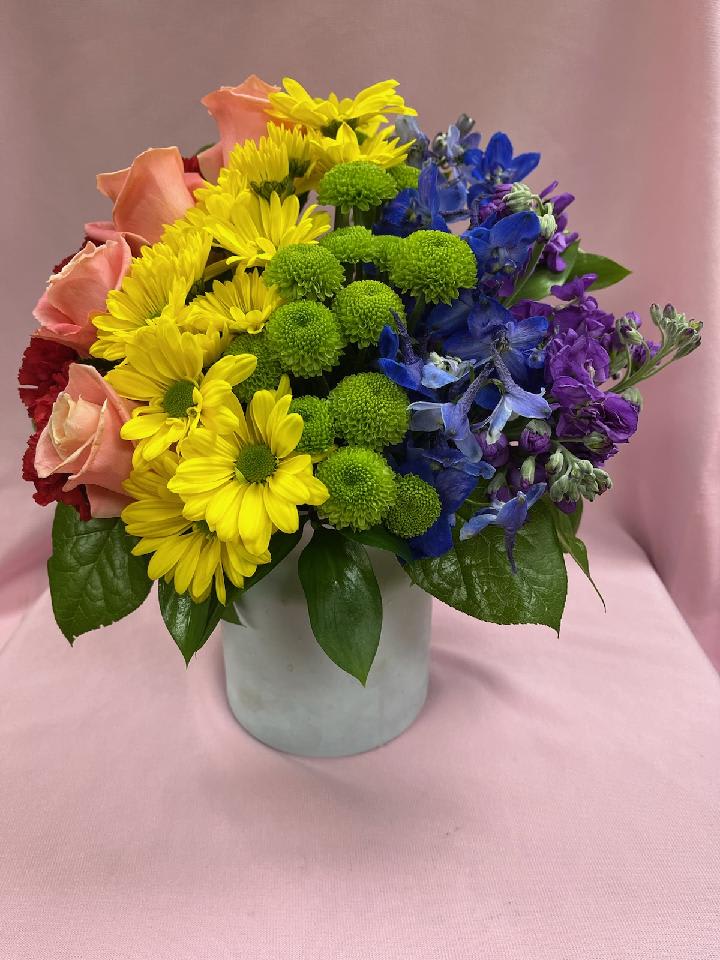 Colorful mixed bouquet in a white vase with yellow, blue, purple, and pink flowers