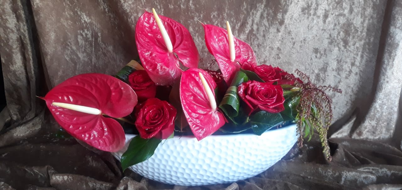 Pink anthuriums and red roses arranged in a white bowl vase