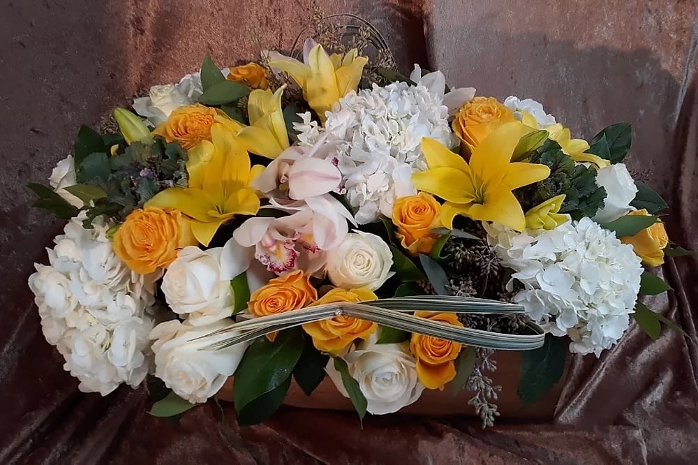 Yellow lilies and orange roses arranged with white blooms in a low container