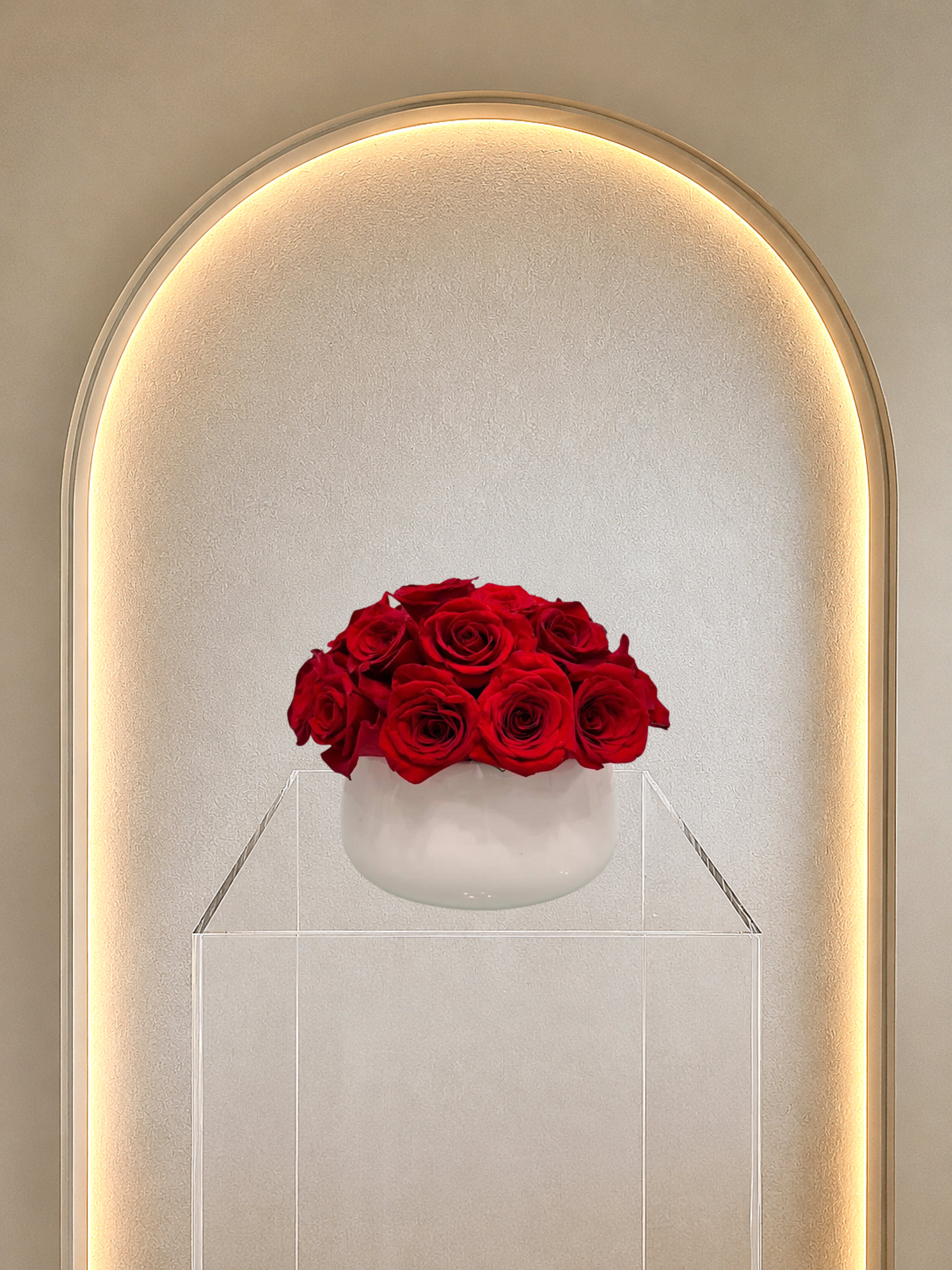 Red Rose Dome - A dense, rounded dome of three dozen vivid red roses creates an immediate impression of classic romance - perfect as an anniversary roses arrangement or a birthday bouquet for the one you love. The tightly packed blooms form a polished, formal silhouette that reads as unmistakably romantic and celebratory; she'll feel deeply seen when presented with this rich display of red roses.  Set in a small white vase and elevated on a clear acrylic stand, the composition has a clean, modern presentation that suits both traditional and contemporary homes. The bouquet's deep red petals are the focal point, contrasted subtly by touches of white and greenery for depth; the compact size makes it ideal for a dining table centerpiece, bedside table, or office desk without overwhelming the space.  Choose this arrangement to mark anniversaries, Valentine's Day, or any moment you want to say "I love you" with timeless elegance. The arrangement arrives ready to display in its white vase; to keep the roses fresh, change the water daily and trim stems slightly every few days.