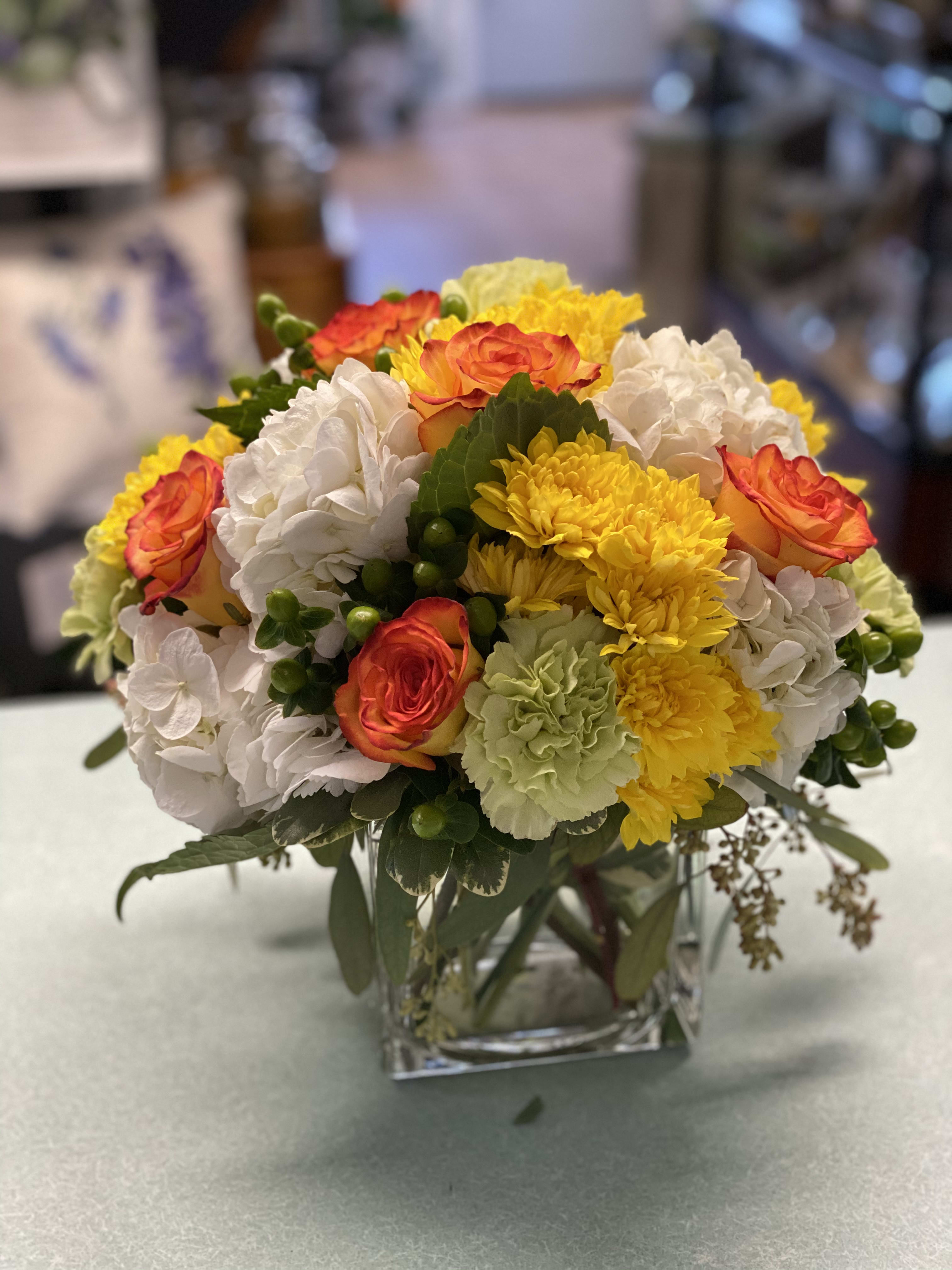 Mixed bouquet of orange roses, white hydrangeas, and yellow chrysanthemums in a glass vase