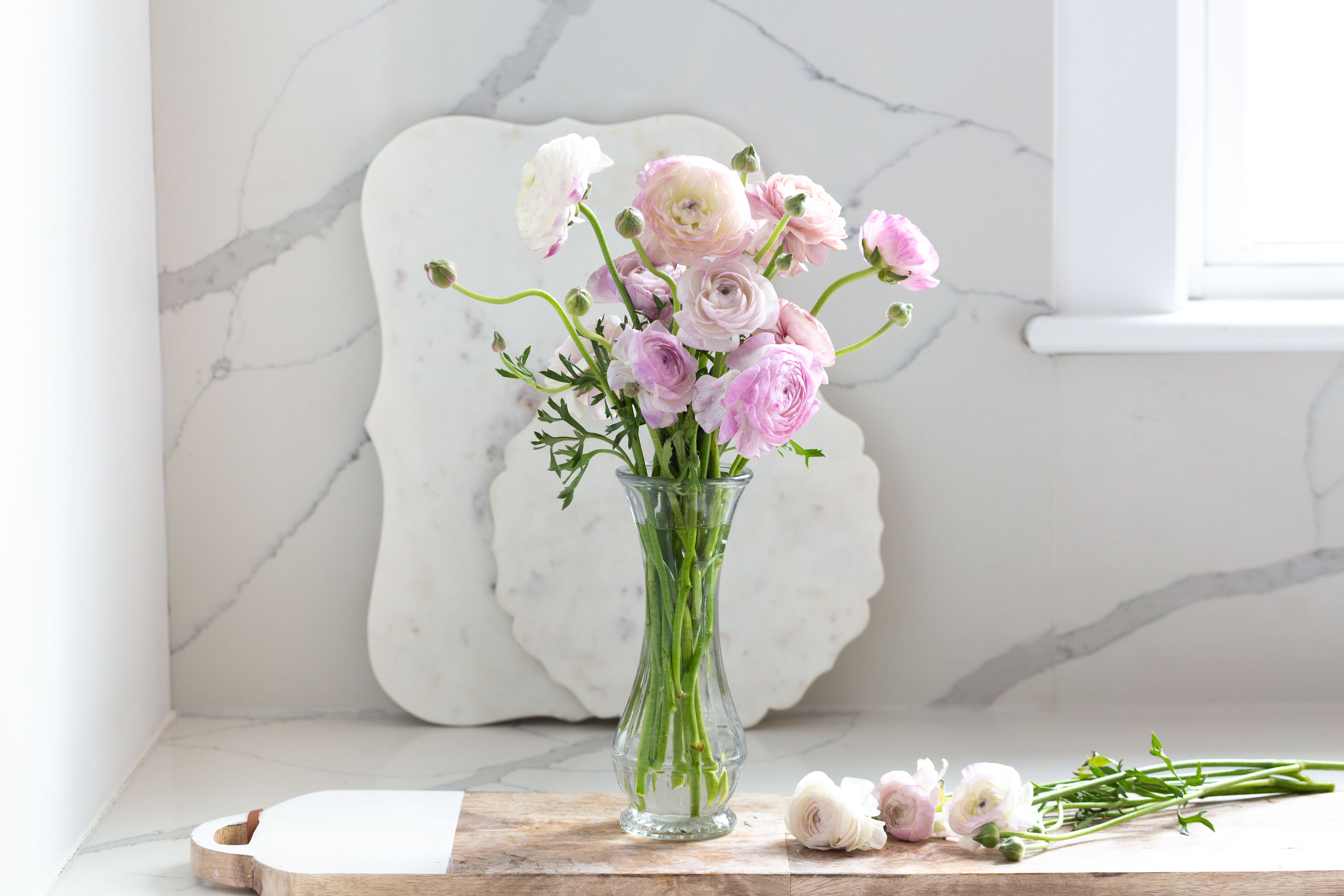 Pink Whisper - Elegant in its simplicity, our Blush Ranunculus Bouquet celebrates one of the season's most beloved blooms. Designed with soft blush, pink, and ivory ranunculus arranged naturally in a clear glass vase, this timeless bouquet brings effortless beauty to any space.  Whether celebrating a birthday, welcoming a new baby, sending thanks, or simply brightening someone's day, this charming arrangement offers a graceful expression of kindness and love.  Each bouquet is handcrafted using the freshest available ranunculus in a soft pastel palette.  Please note: Ranunculus are seasonal flowers. When available, your bouquet will feature premium ranunculus in soft shades of blush, pink, peach, white, or other complementary pastel tones. If ranunculus are out of season or unavailable, we may substitute them with premium garden-style roses or similar blooms of equal beauty and value while preserving the overall color palette and natural, airy design.