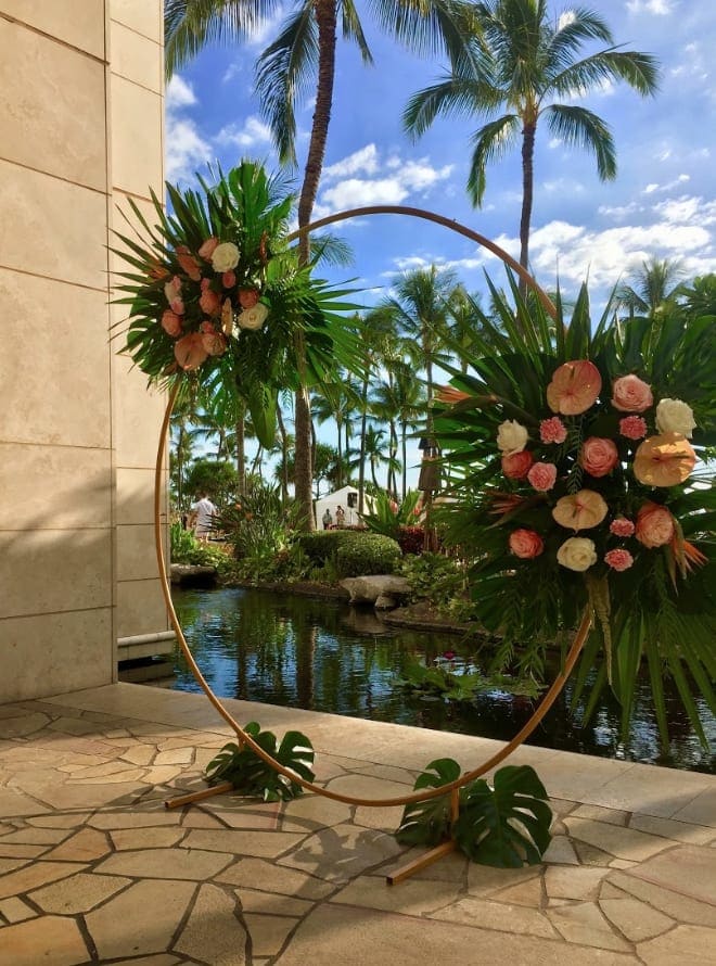 Two floral arrangements on a circular stand beside a tropical pool