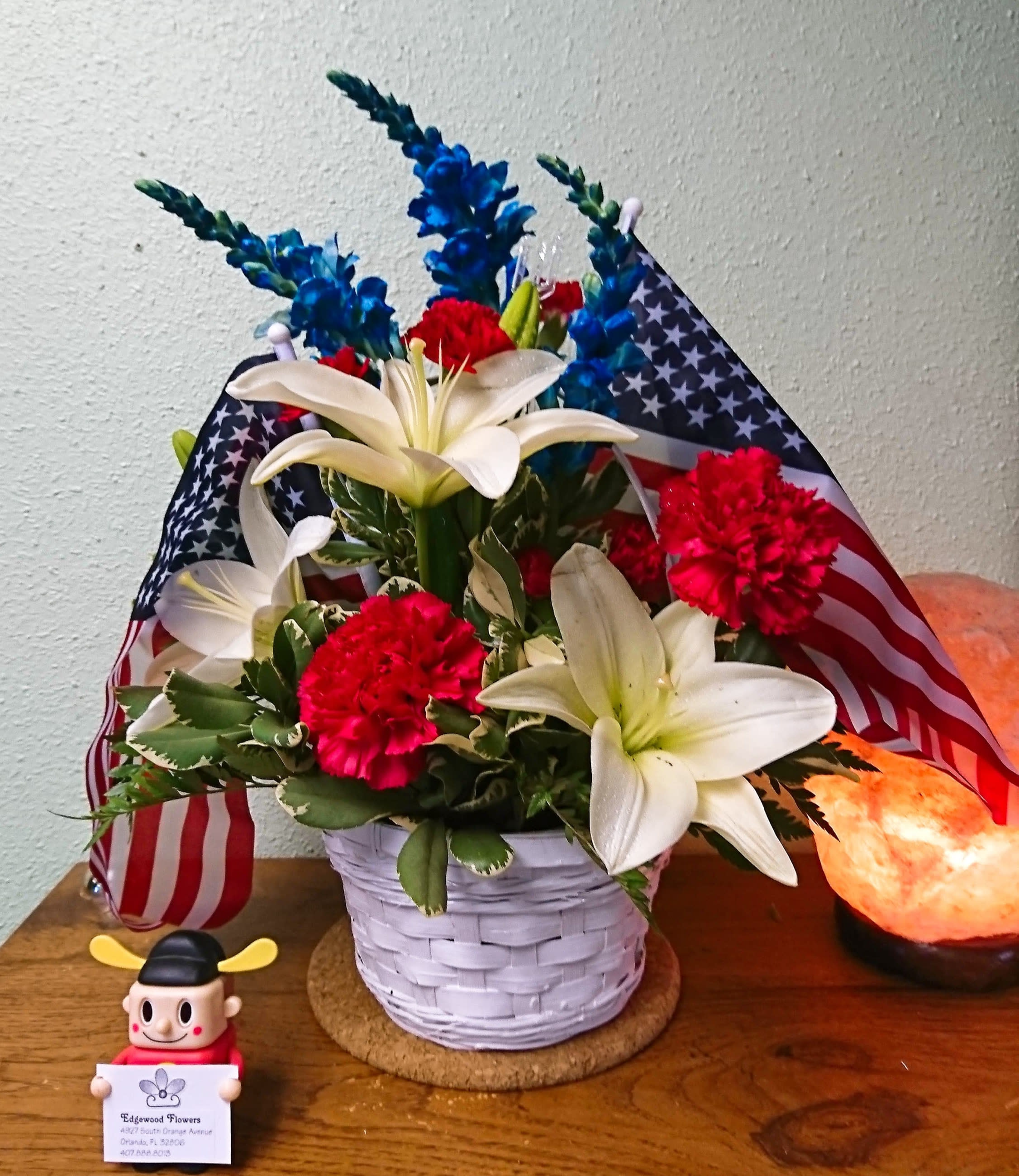 Basket arrangement with white lilies, red carnations, and blue flowers with American flags