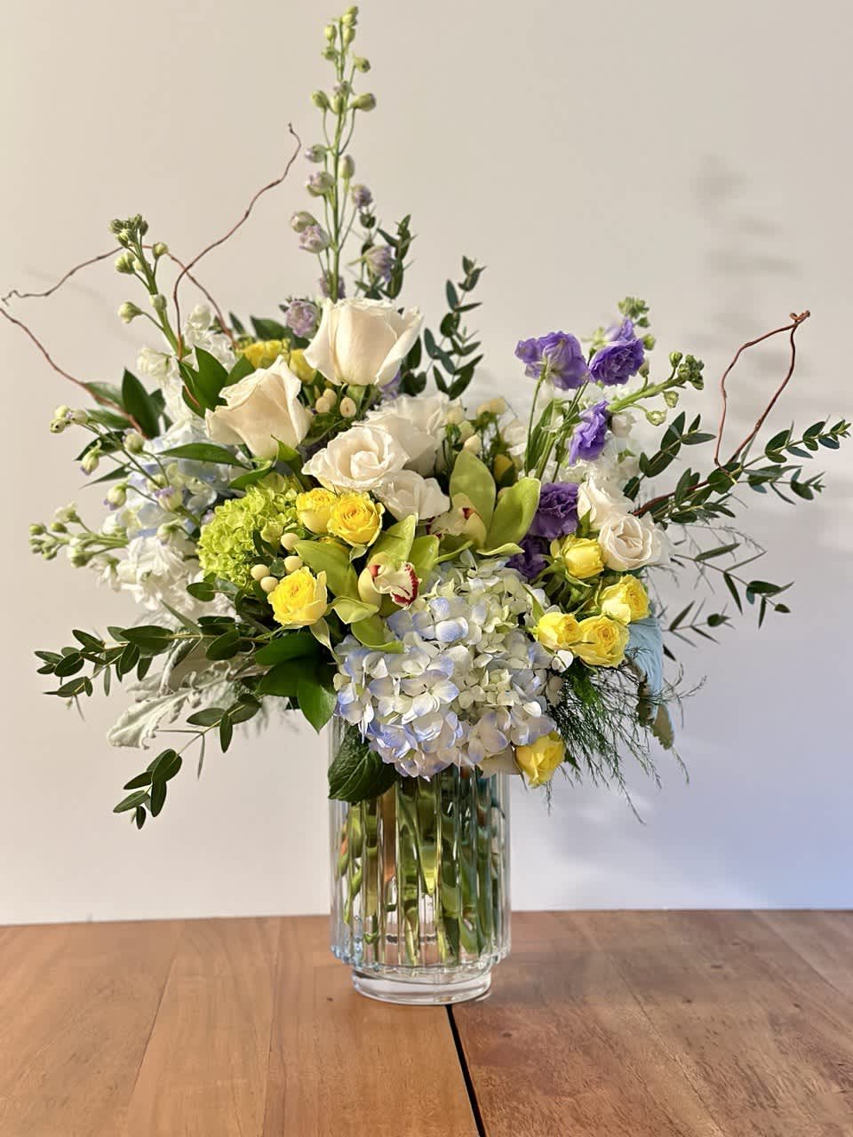 Mixed bouquet of white, yellow, purple, and blue flowers in a glass vase