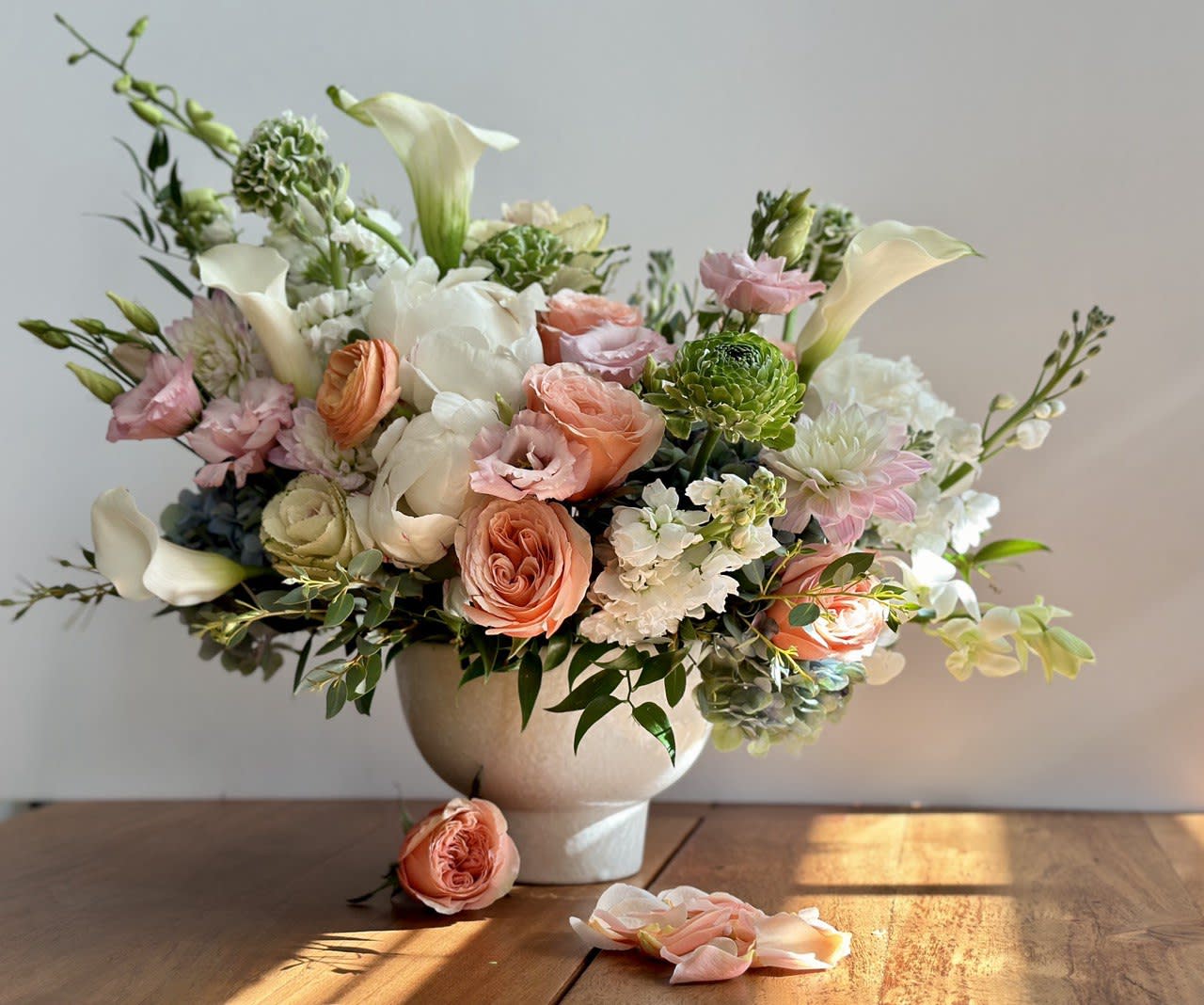 Pastel floral arrangement in a white vase with roses and calla lilies