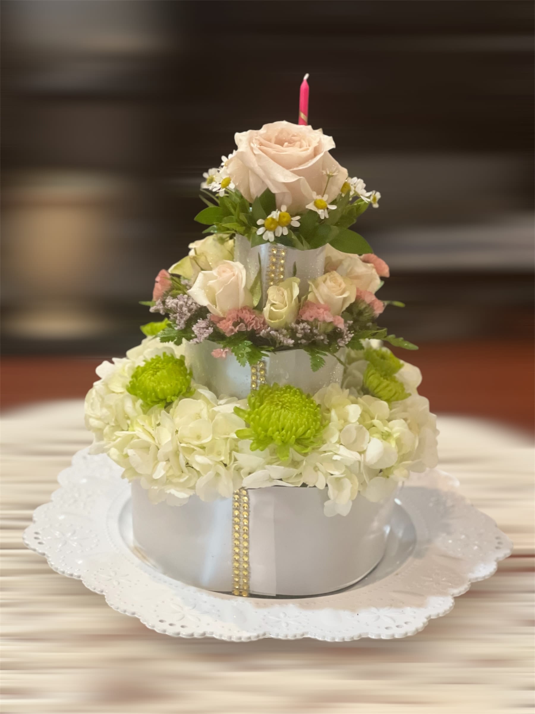 Tiered floral cake with cream roses and white hydrangeas on a doily-lined plate