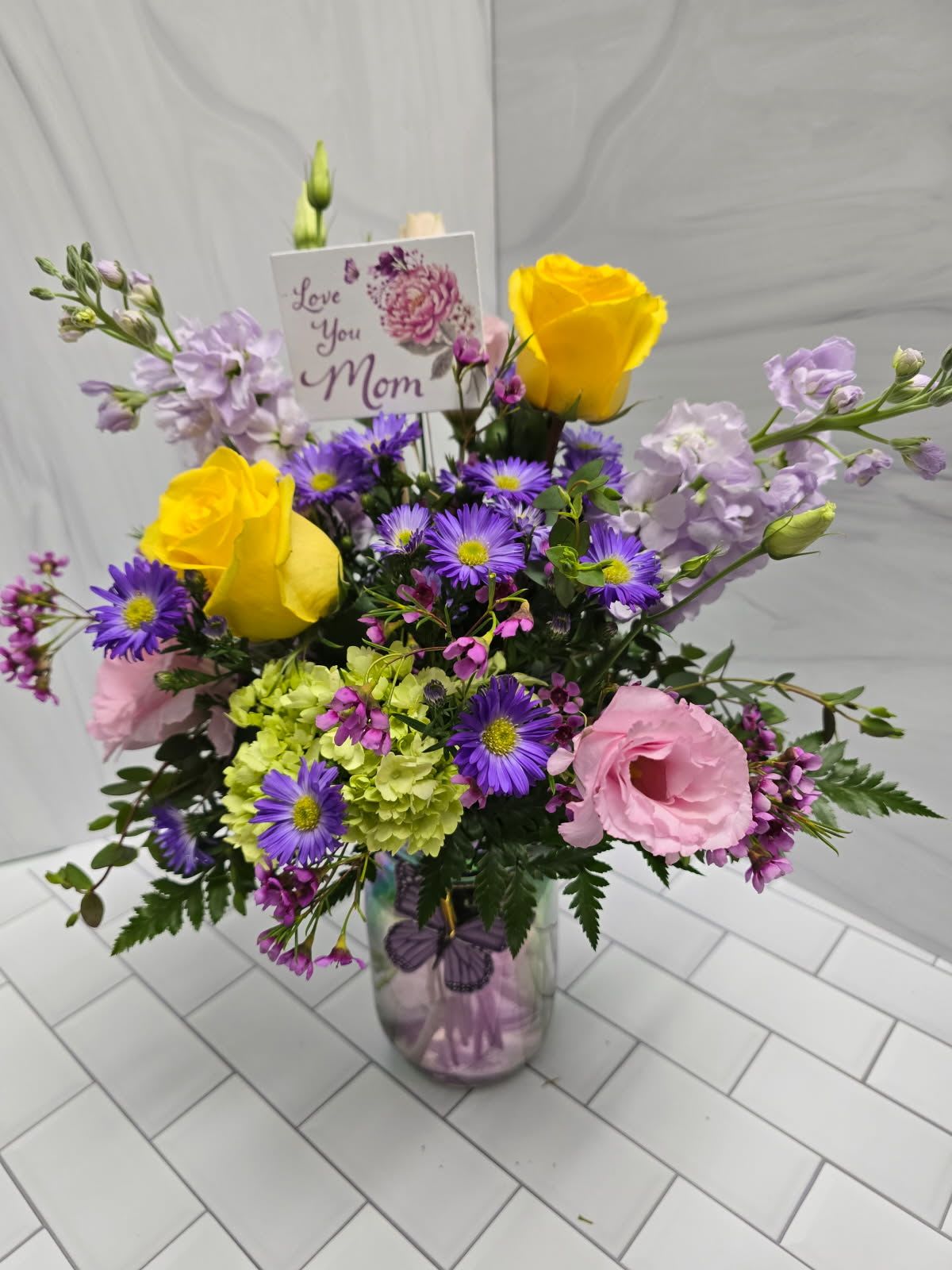 Mixed bouquet in a glass vase with yellow roses, pink blooms, and purple daisies