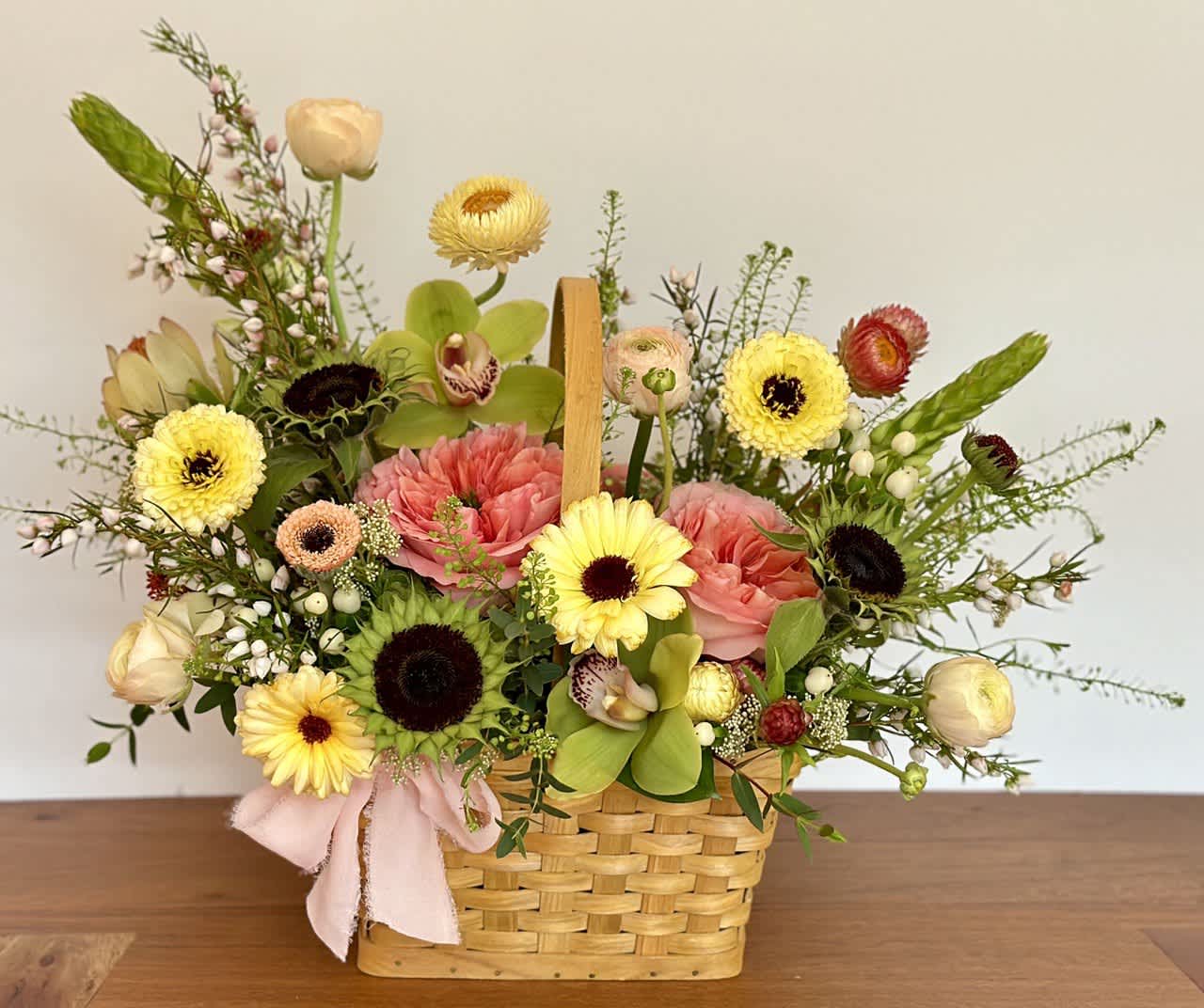 Mixed flower arrangement in a woven basket with a pink ribbon