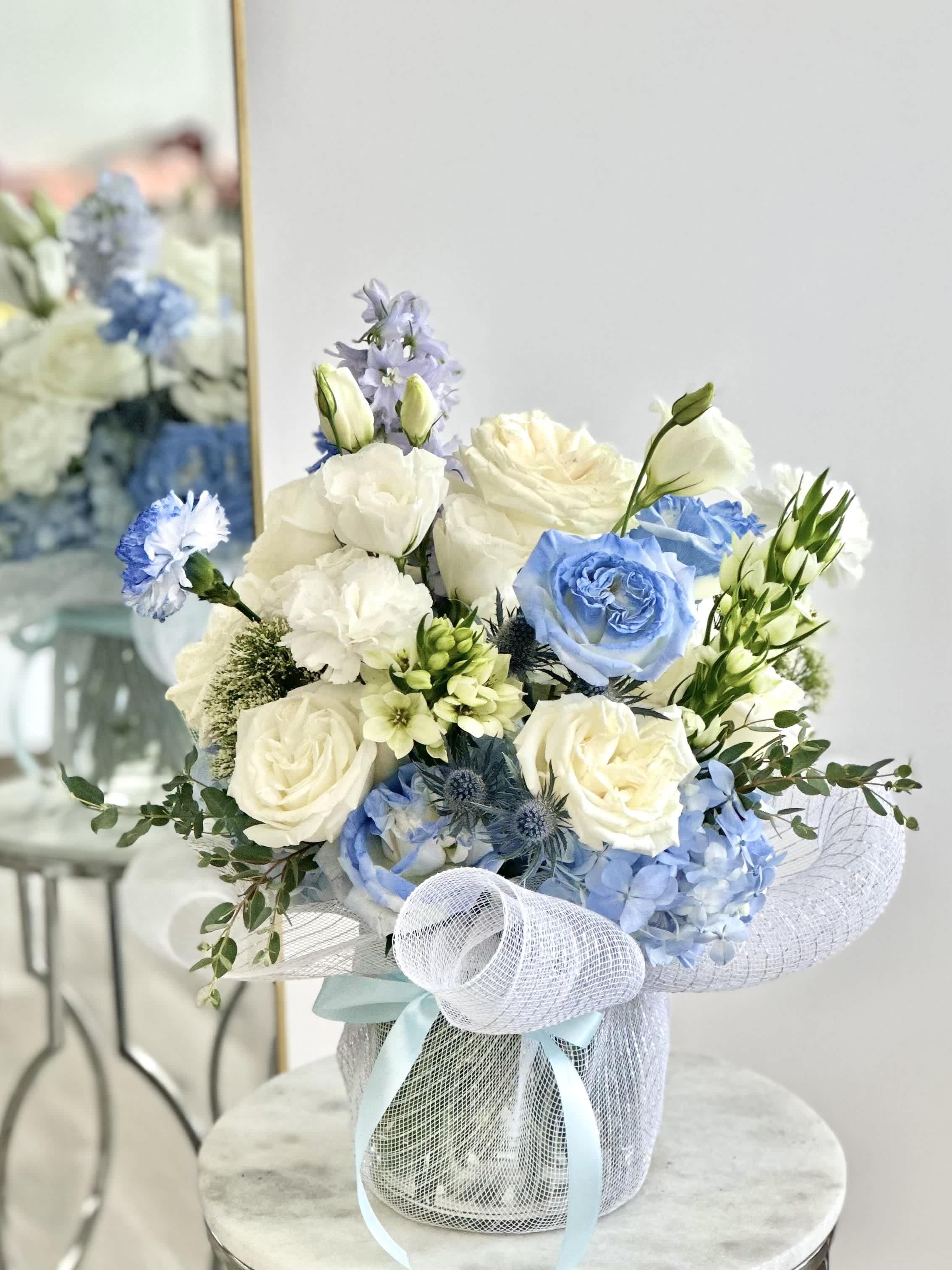 Ocean - A medium cylinder glass vase with white and light blue flowers.   Flower types may vary depending on the season.