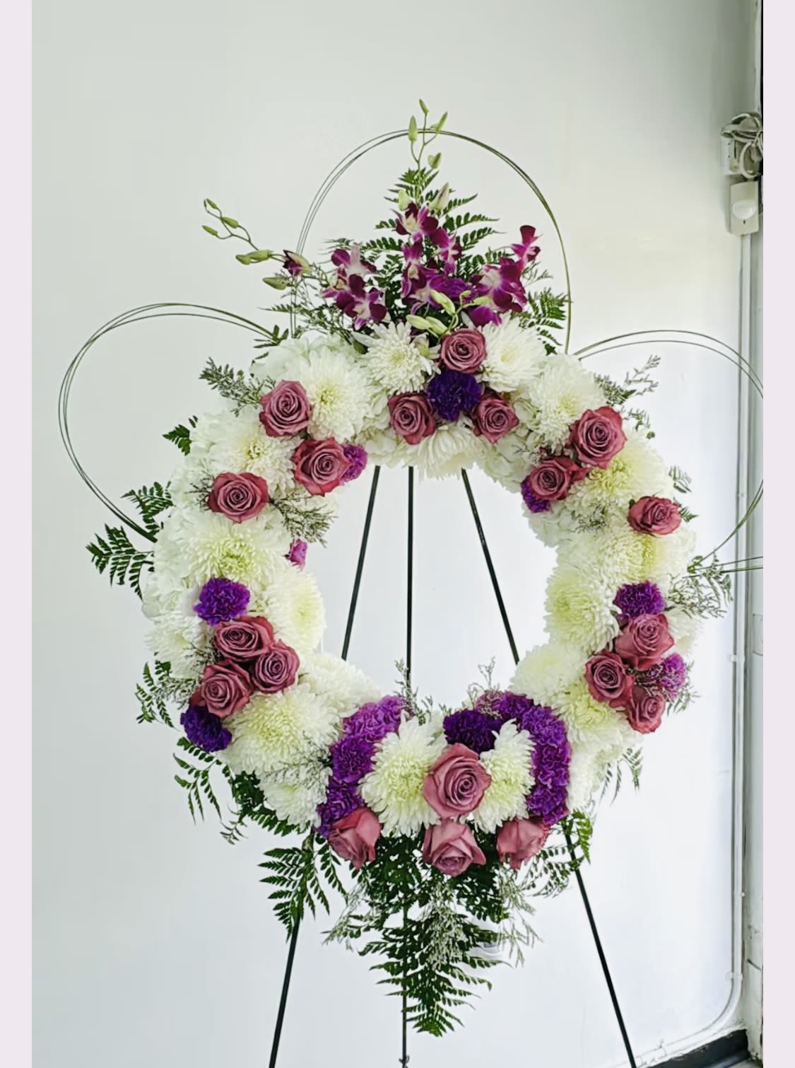 Large floral wreath on a stand with pink roses, white mums, and purple flowers