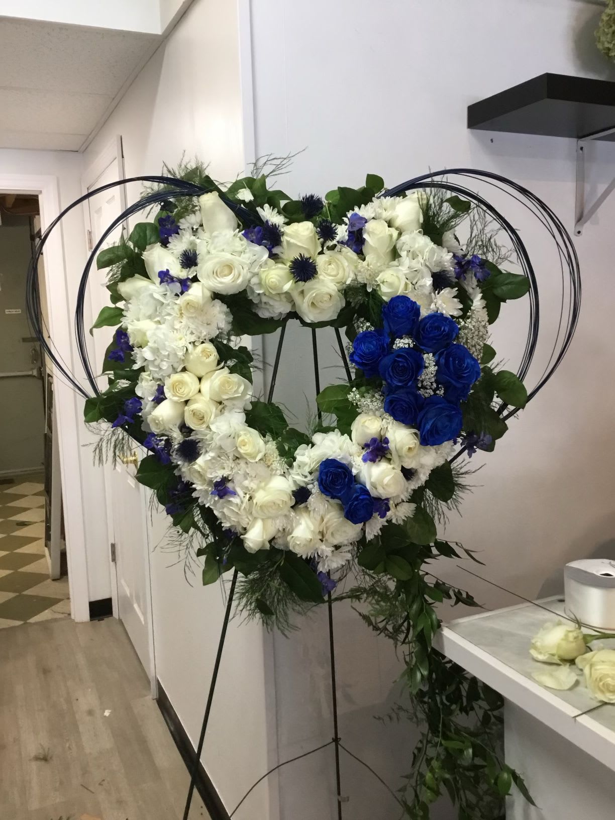 Heart-shaped floral wreath with white and blue roses on a stand