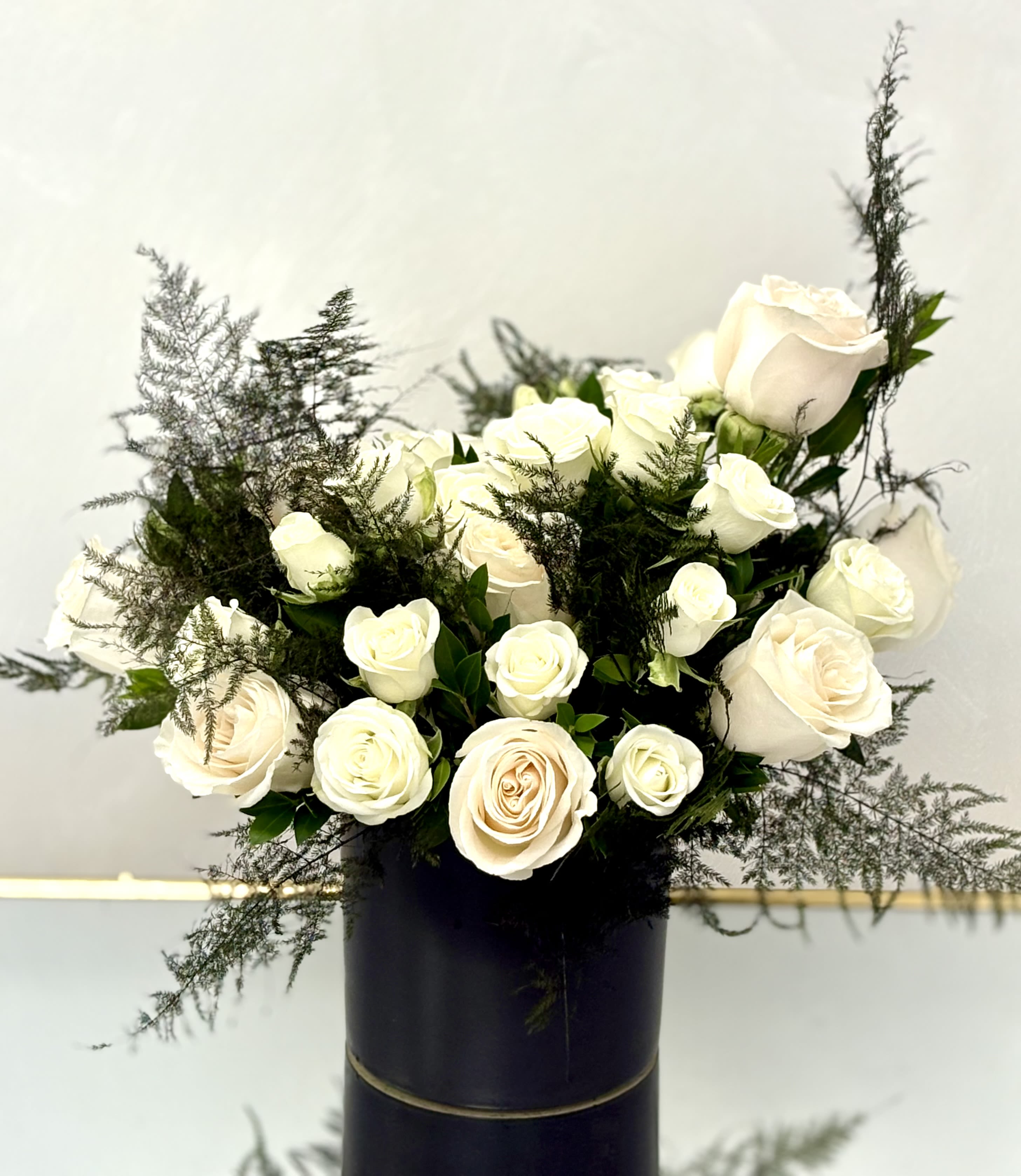 Arrangement of white roses with airy greenery in a tall black cylinder vase