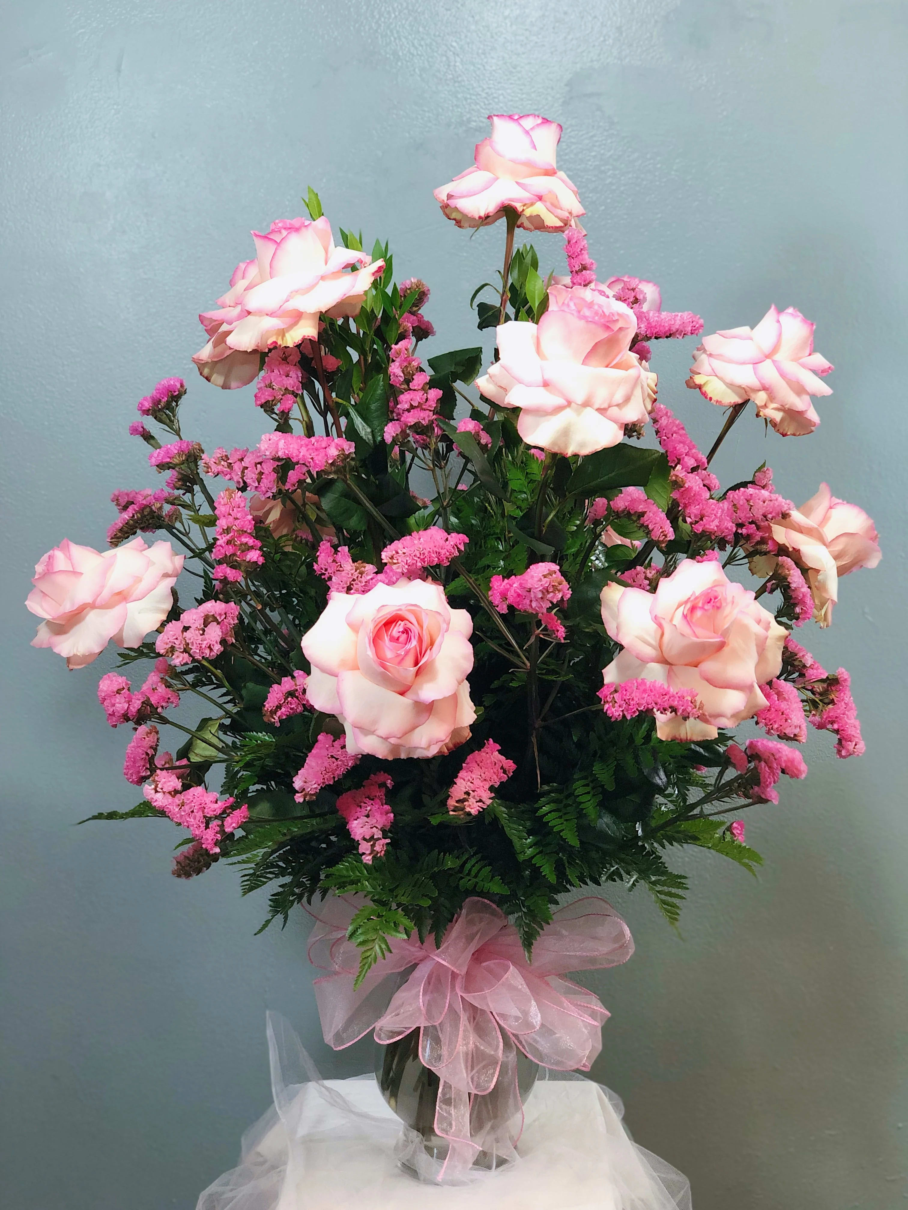 Tall arrangement of pink roses and pink filler flowers in a glass vase with a pink bow
