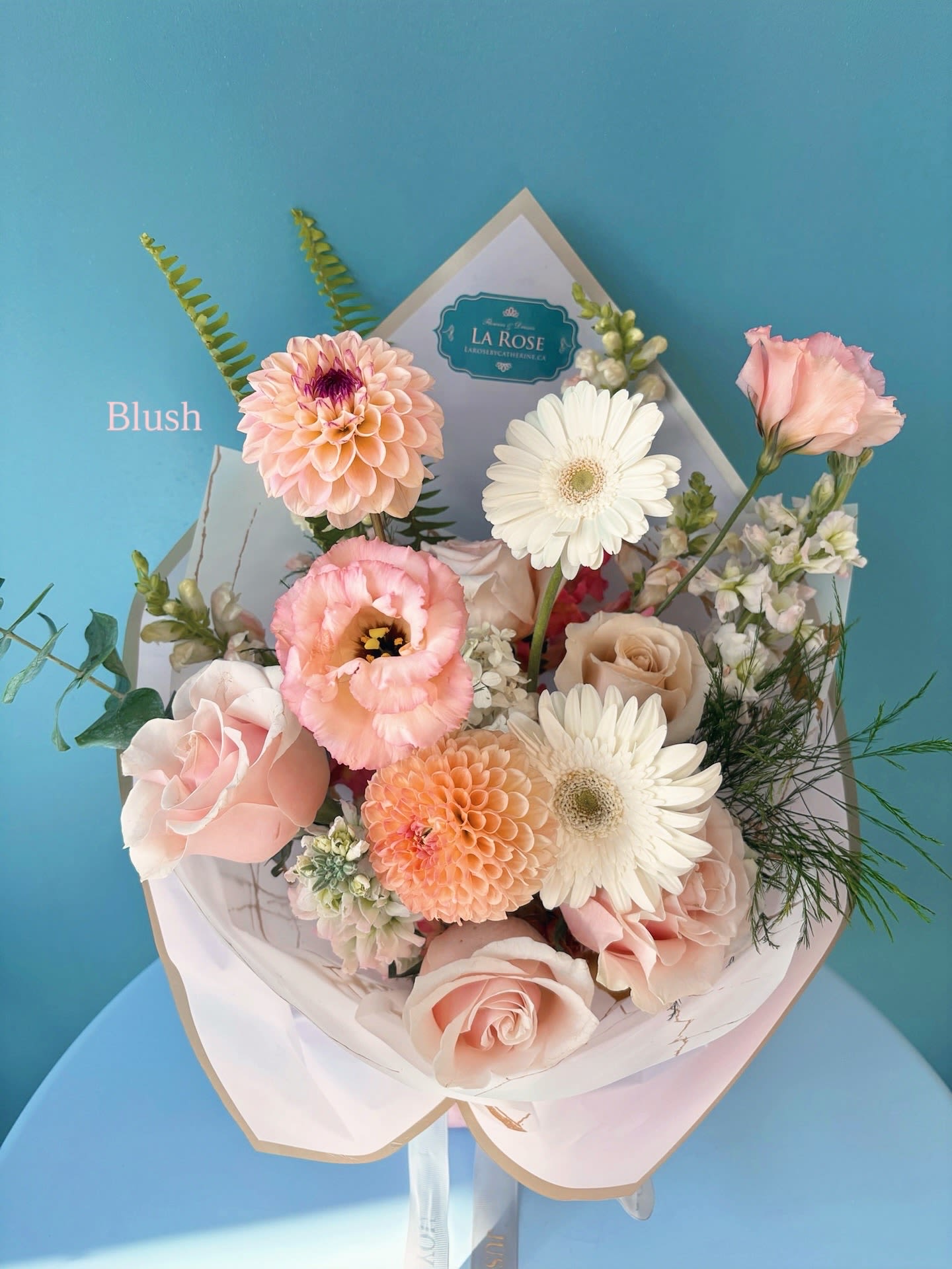 Blush bouquet with roses, gerbera daisies, and peach blooms in white wrap