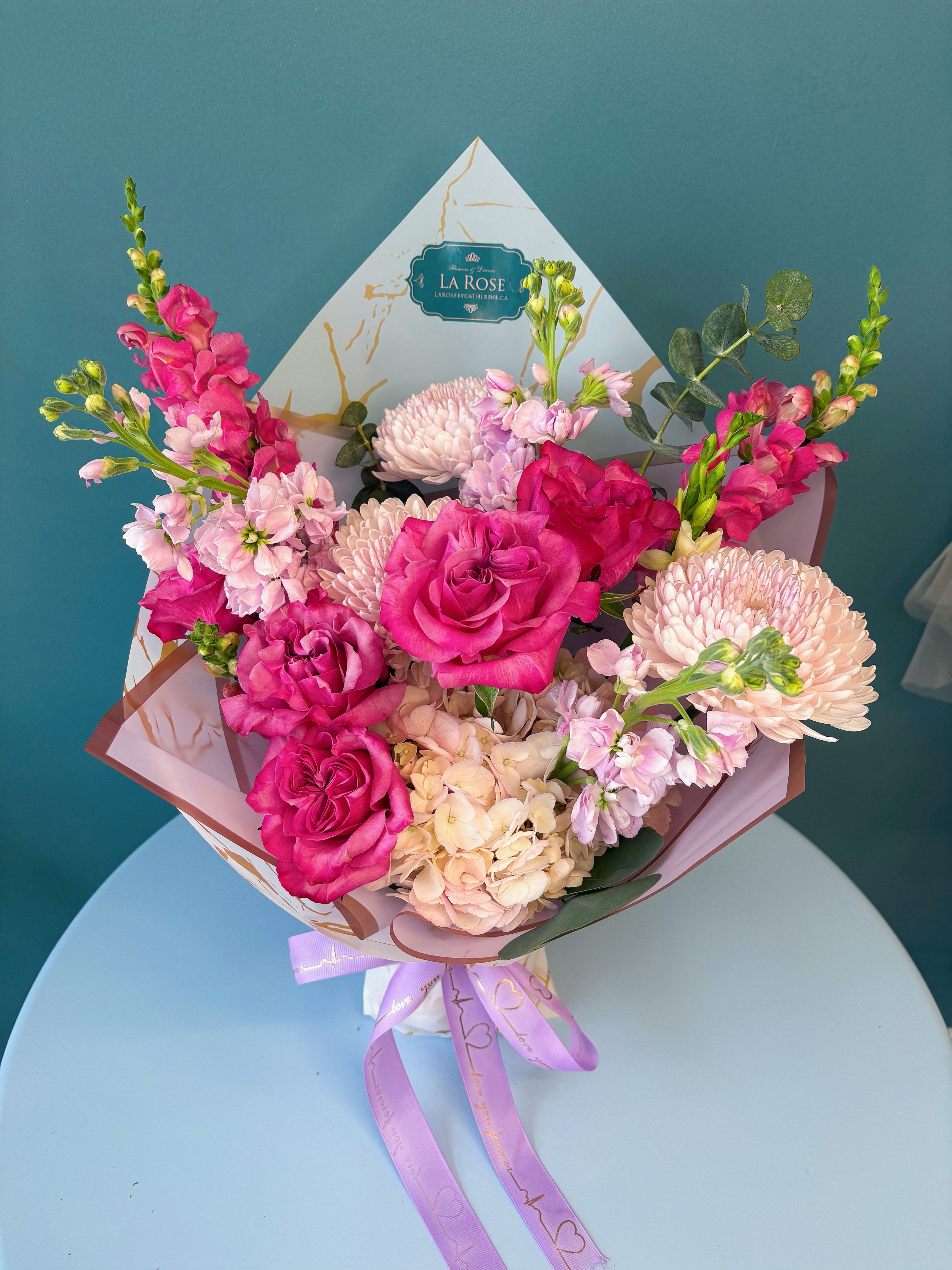 Pink roses and pale chrysanthemums in a wrapped bouquet with a lavender ribbon