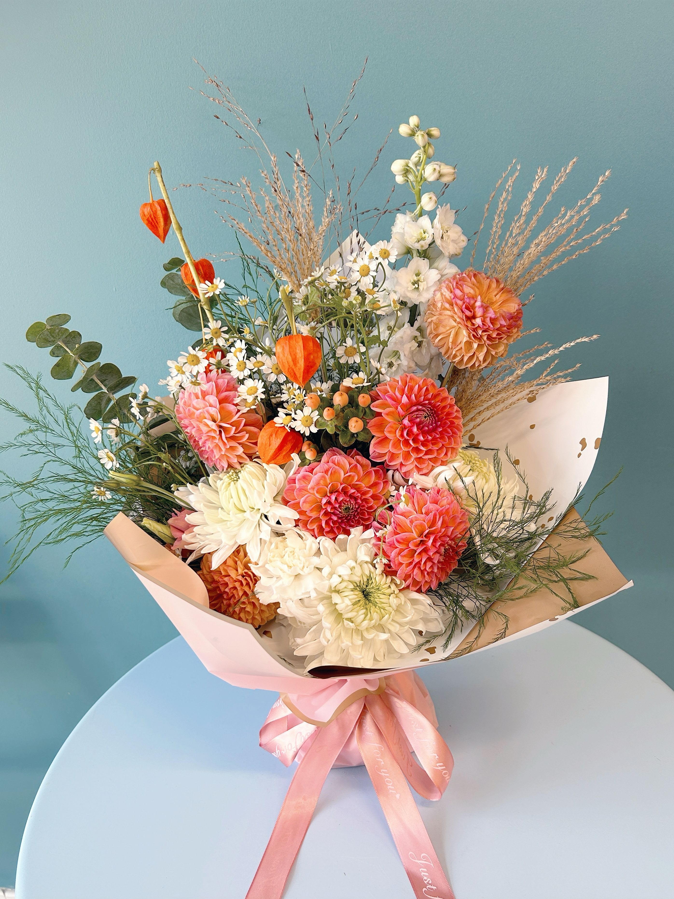 Mixed bouquet of pink, white, and orange flowers with a pink ribbon wrap