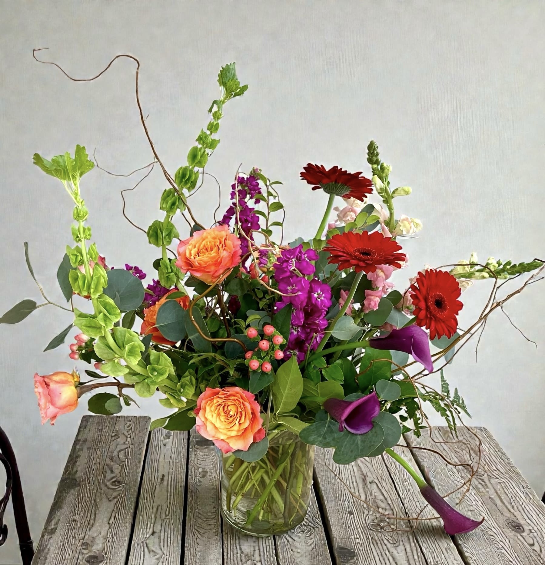 Audacious - Orange roses and bright red gerbera daisies take center stage in this tall, sculptural flower arrangement. Perfect as a birthday bouquet, congratulations gift, or a cheerful thank-you surprise for someone who loves bold color. 