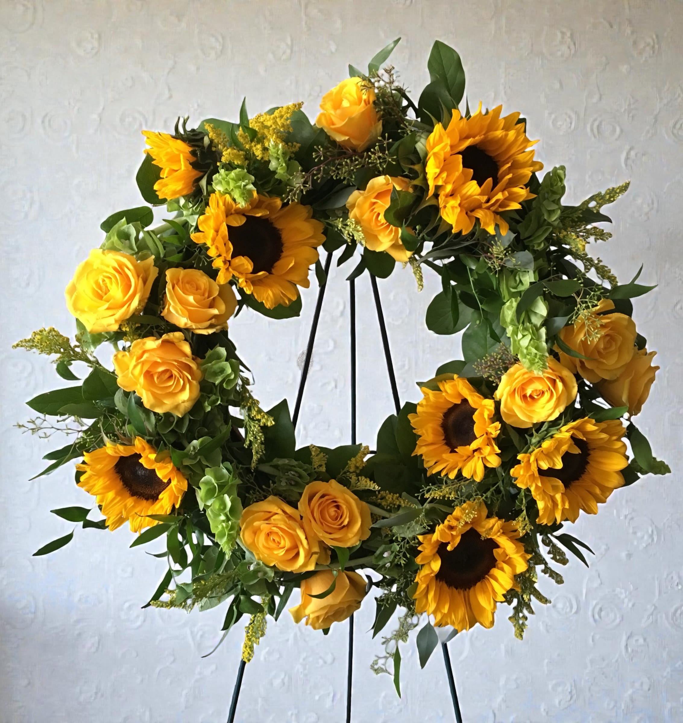 Beaming Wreath - Sunflowers and yellow roses arranged in a bright circular wreath with greenery create an uplifting sympathy and funeral tribute with fresh, sunny tones.