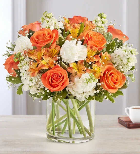 Orange roses and white flowers arranged in a clear glass vase