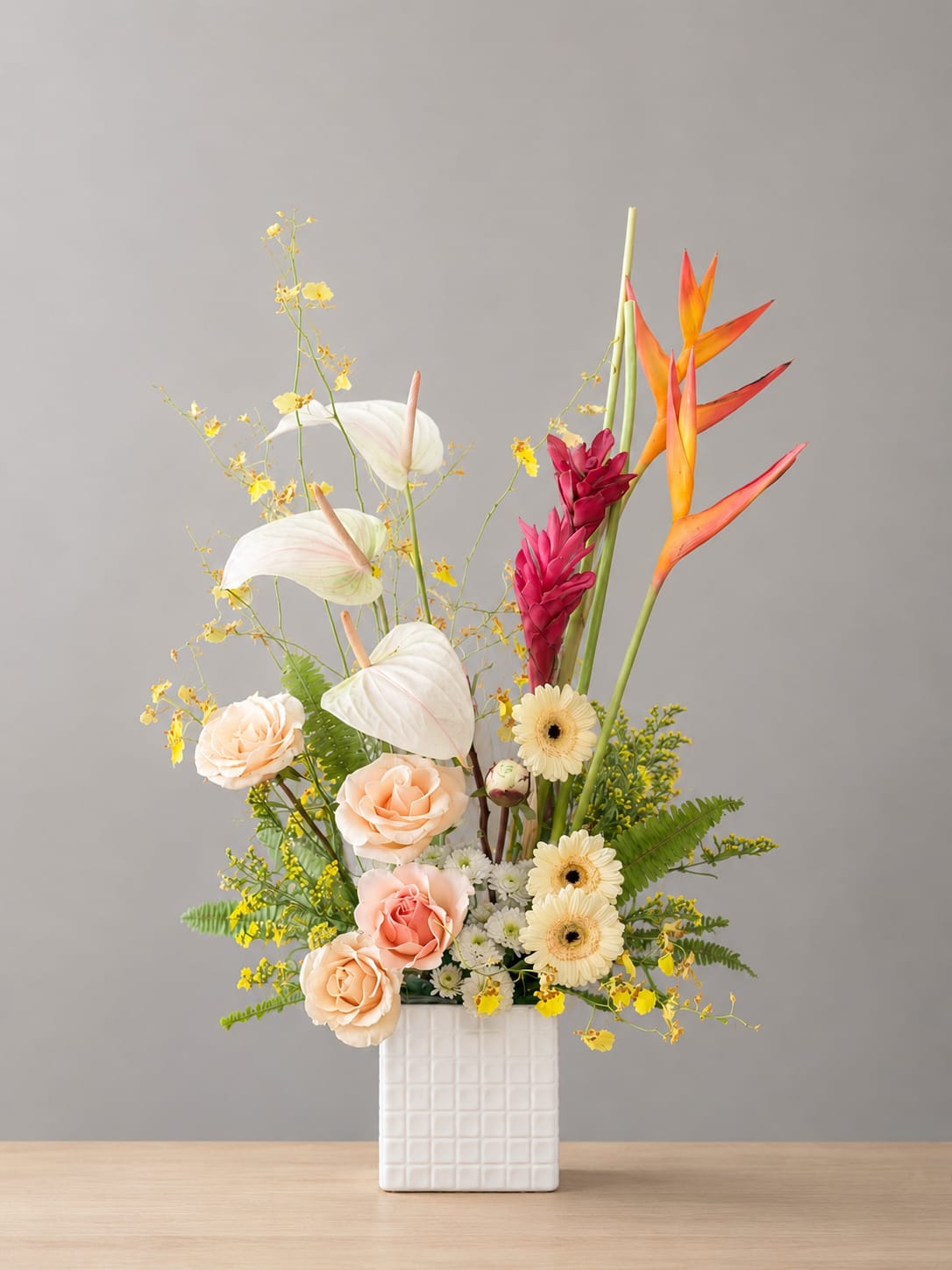 Island Breeze - Tall white anthuriums and orange-red bird-of-paradise create an immediate island feel in this tropical bouquet, making it a striking choice for a birthday bouquet or warm-weather celebration. The upright composition pairs that dramatic height with soft blush and peach roses so the person you're thinking of will feel both celebrated and cared for - vibrant and elegant at once.   The color story - white, pink, orange and yellow - keeps the design lively without feeling cluttered.  Perfect for gifting to someone who loves contemporary, vacation-inspired style, this piece works well as a centerpiece for a festive event or as a standout arrangement to mark an anniversary or congratulations moment. The rigid square ceramic vase gives stable support for the taller stems; no special care beyond fresh water and a cool spot away from direct sun will keep the arrangement looking its best.
