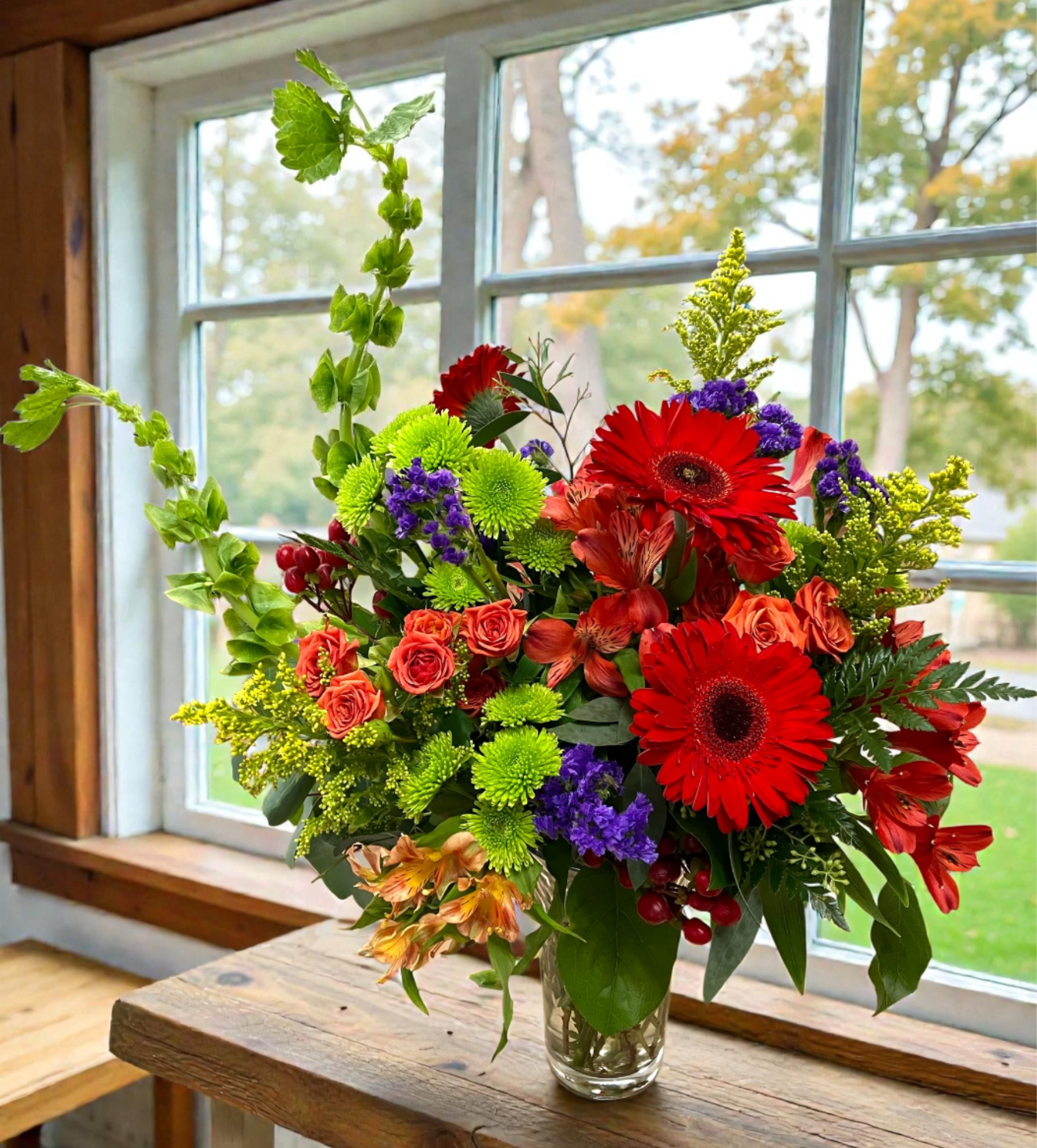 Bright mixed bouquet in a clear glass vase with red gerbera daisies and orange roses