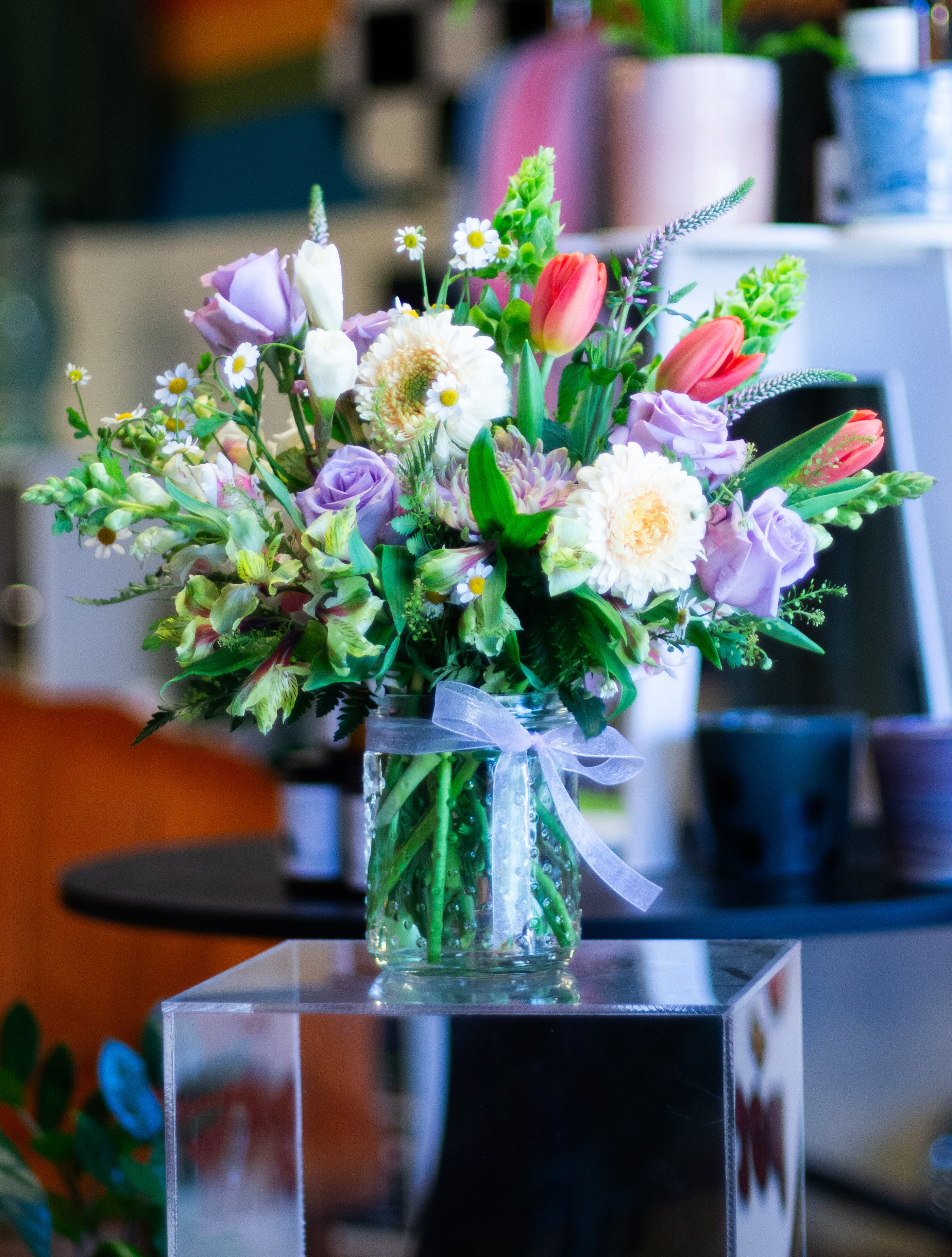 Mixed bouquet of pastel flowers in a glass vase with a ribbon