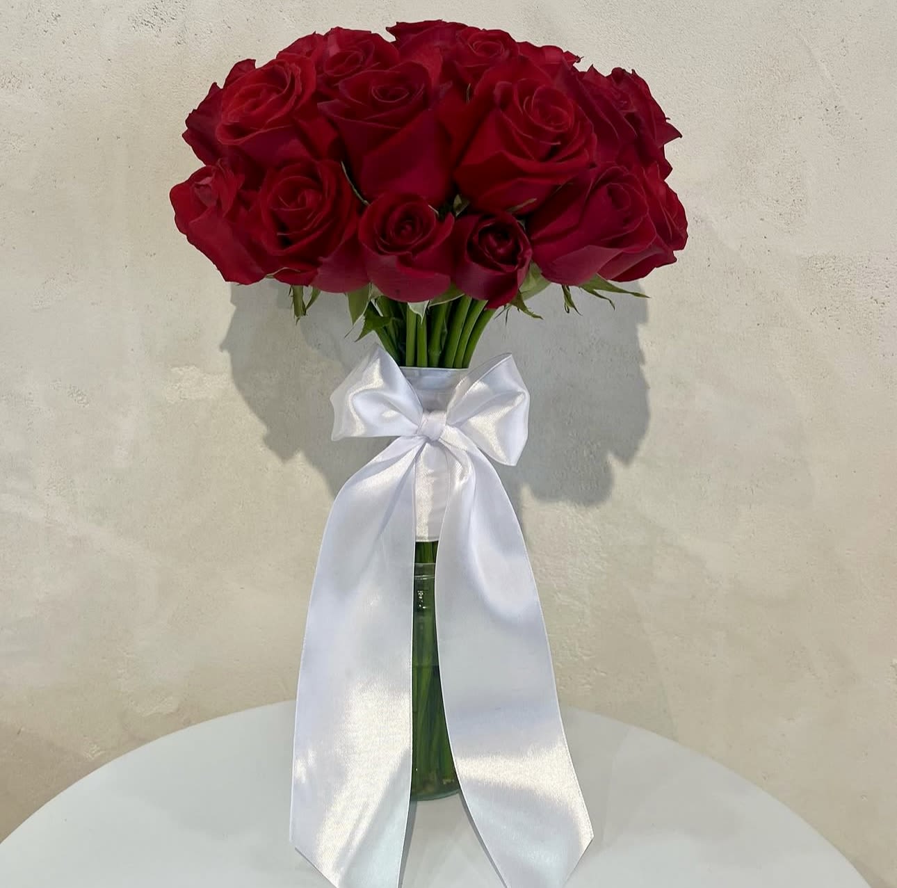 Bouquet of red roses in a glass vase with a white ribbon bow