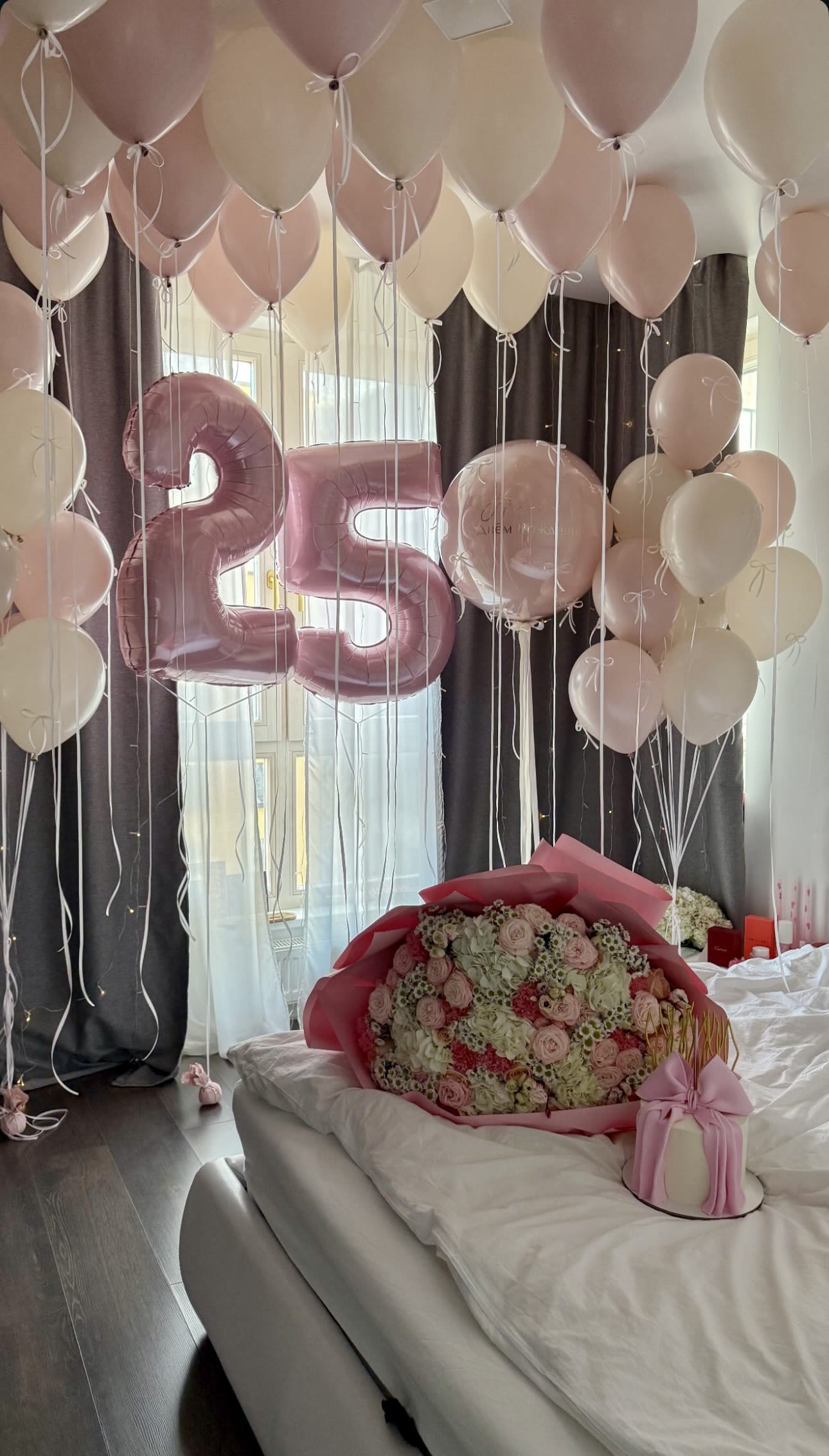 Pink and white balloons with a large 25 balloon above a bouquet on a bed