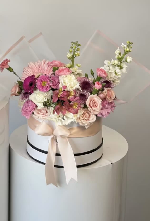 Pink and white mixed flower arrangement in a round hat box with ribbon