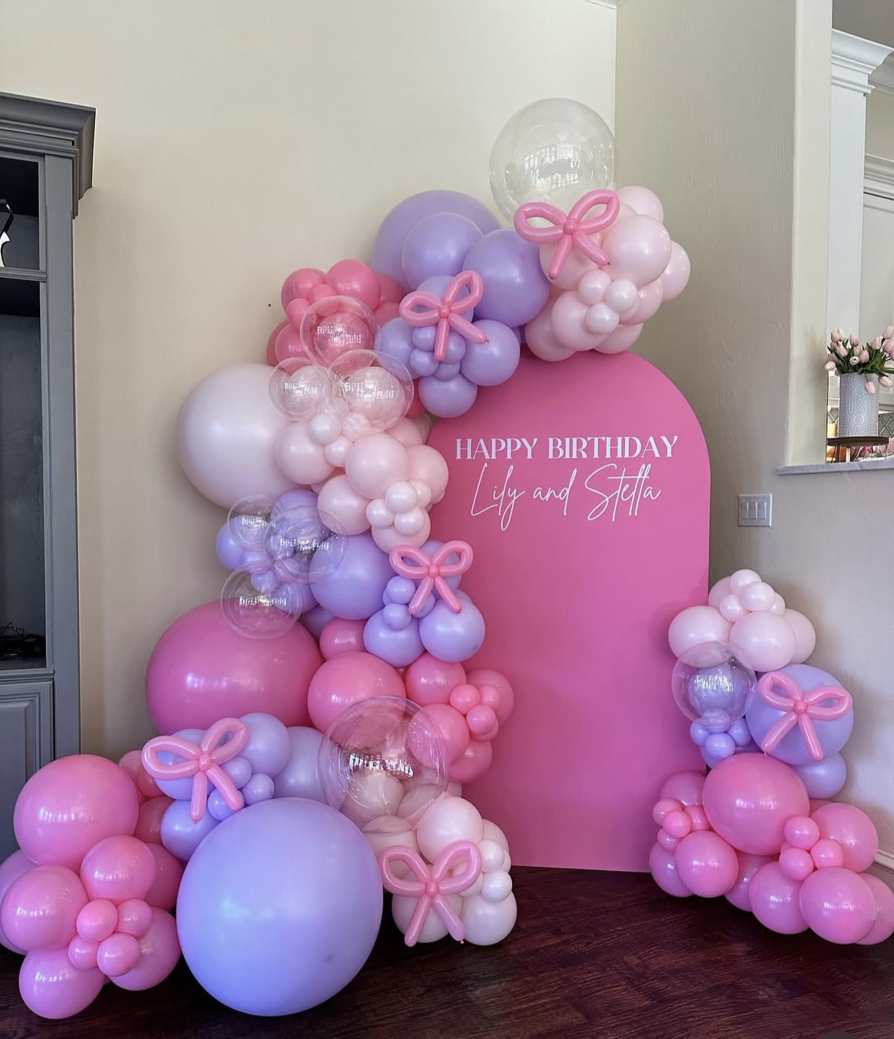Pink and lavender balloon birthday display with a large sign reading Happy Birthday Lily and Stella