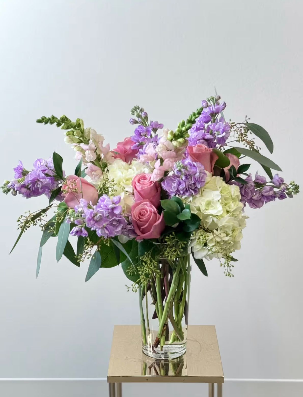 Pink roses and purple flowers in a clear glass vase