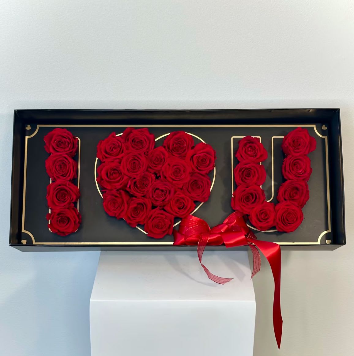 Red roses arranged in a black box to spell "I LOVE U" with a red ribbon