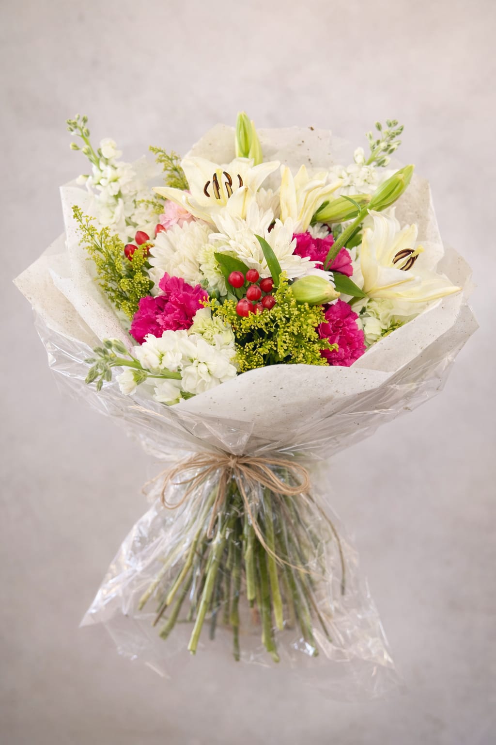 Bouquet of white lilies, pink carnations, and white chrysanthemums wrapped in paper