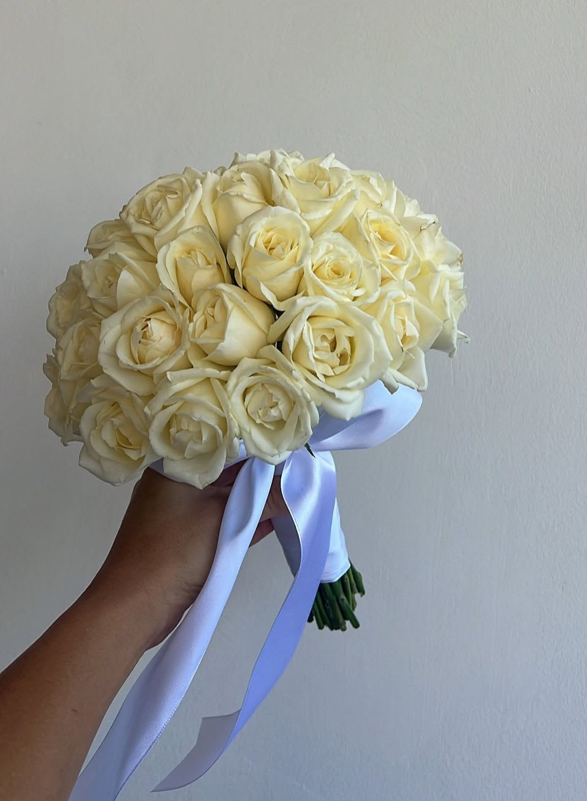 Handheld bouquet of cream roses tied with a pale ribbon