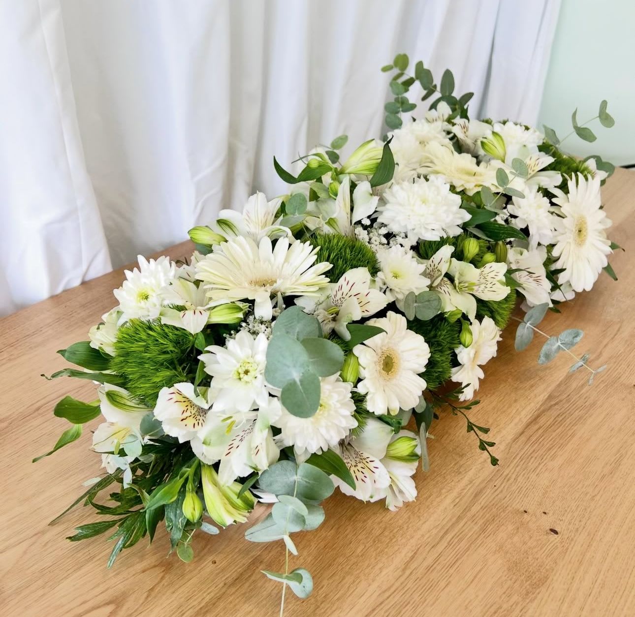 White floral arrangement with daisies and lilies on a wooden table