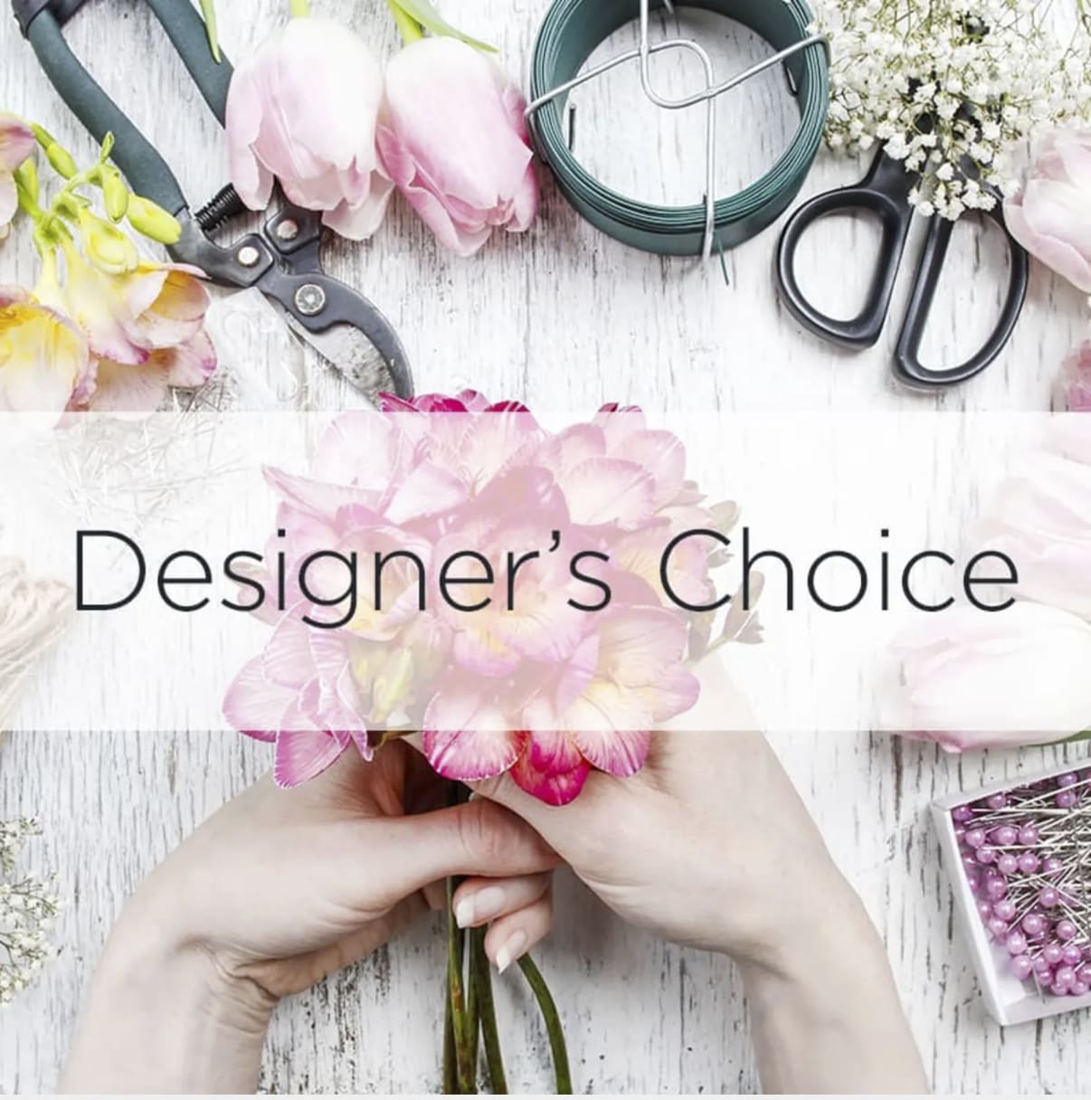 Hands hold a pink flower bouquet with floral tools and supplies around it.