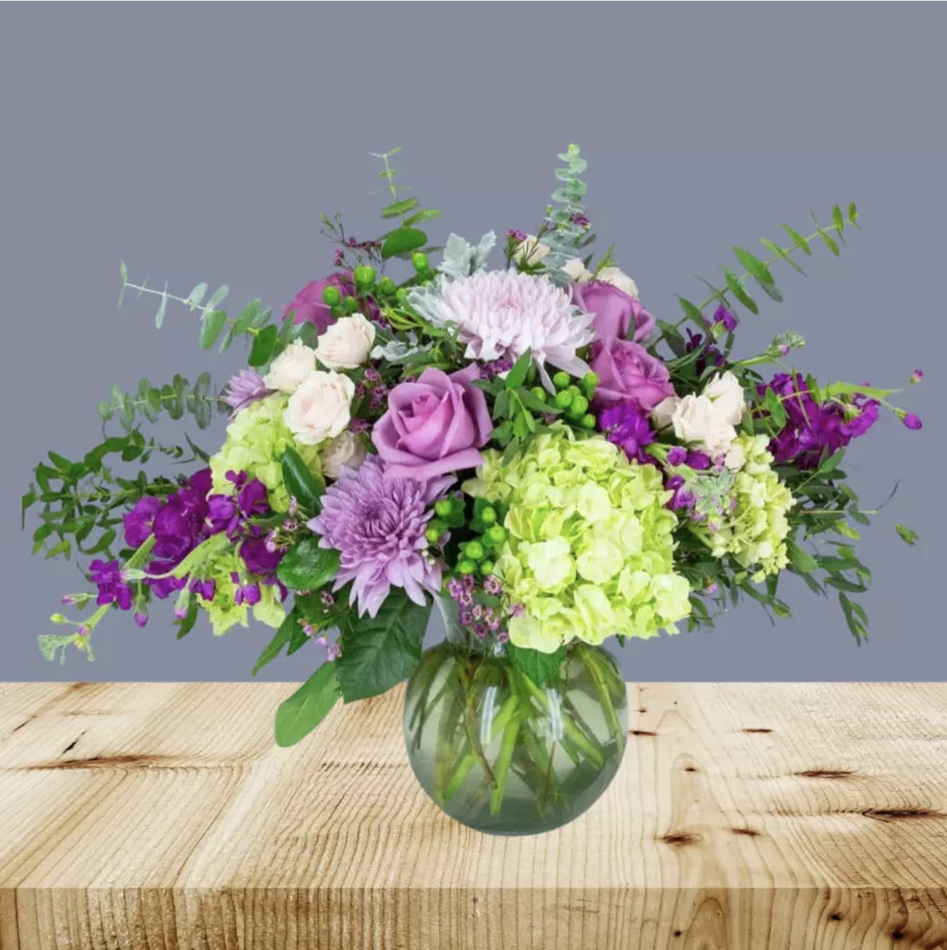 Mixed bouquet of purple, pink, white, and green flowers in a glass vase
