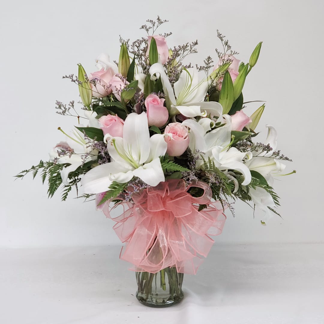 Pink roses and white lilies in a glass vase with a pink bow