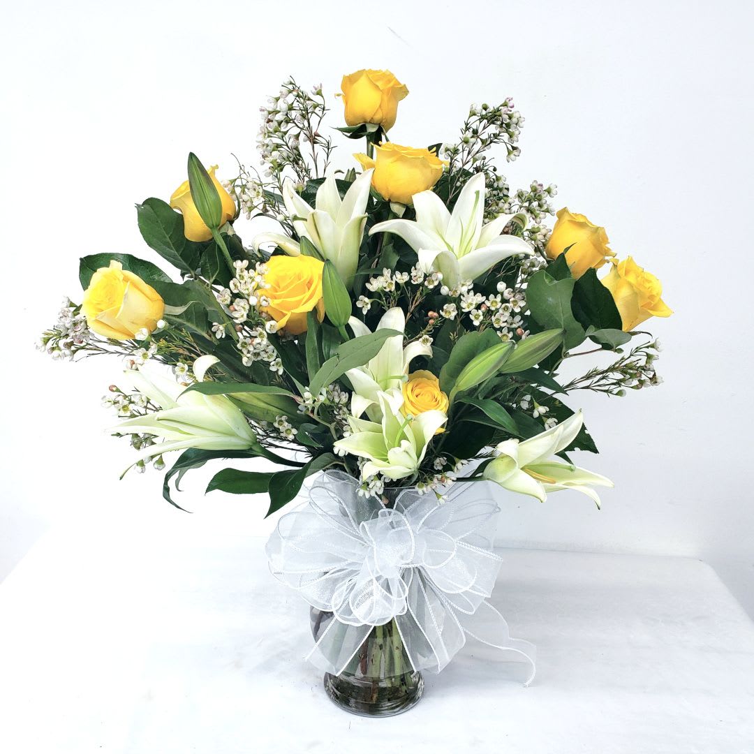 Yellow roses and white lilies in a glass vase with a white bow