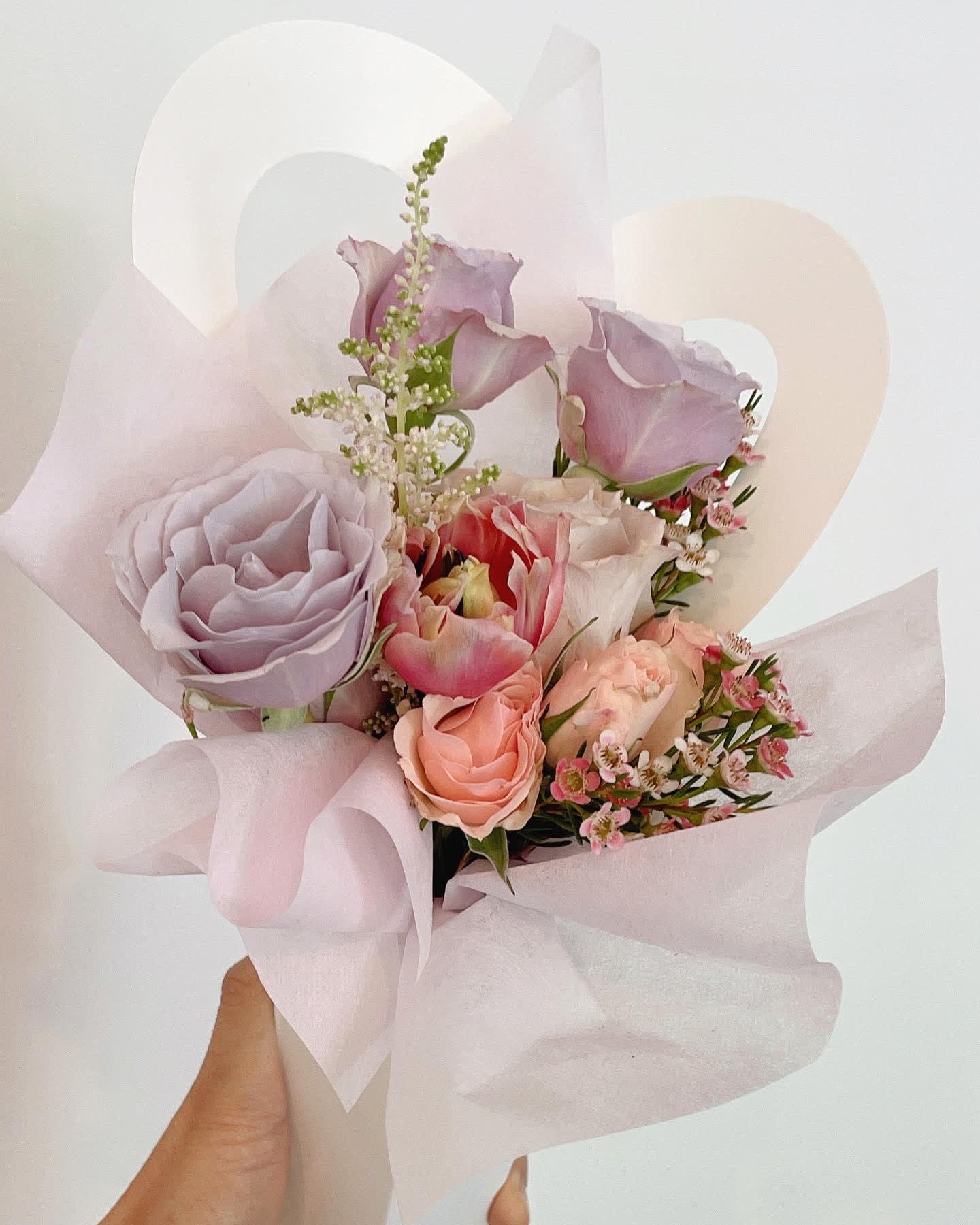 Handheld bouquet of pastel roses and tulips wrapped in pale pink paper