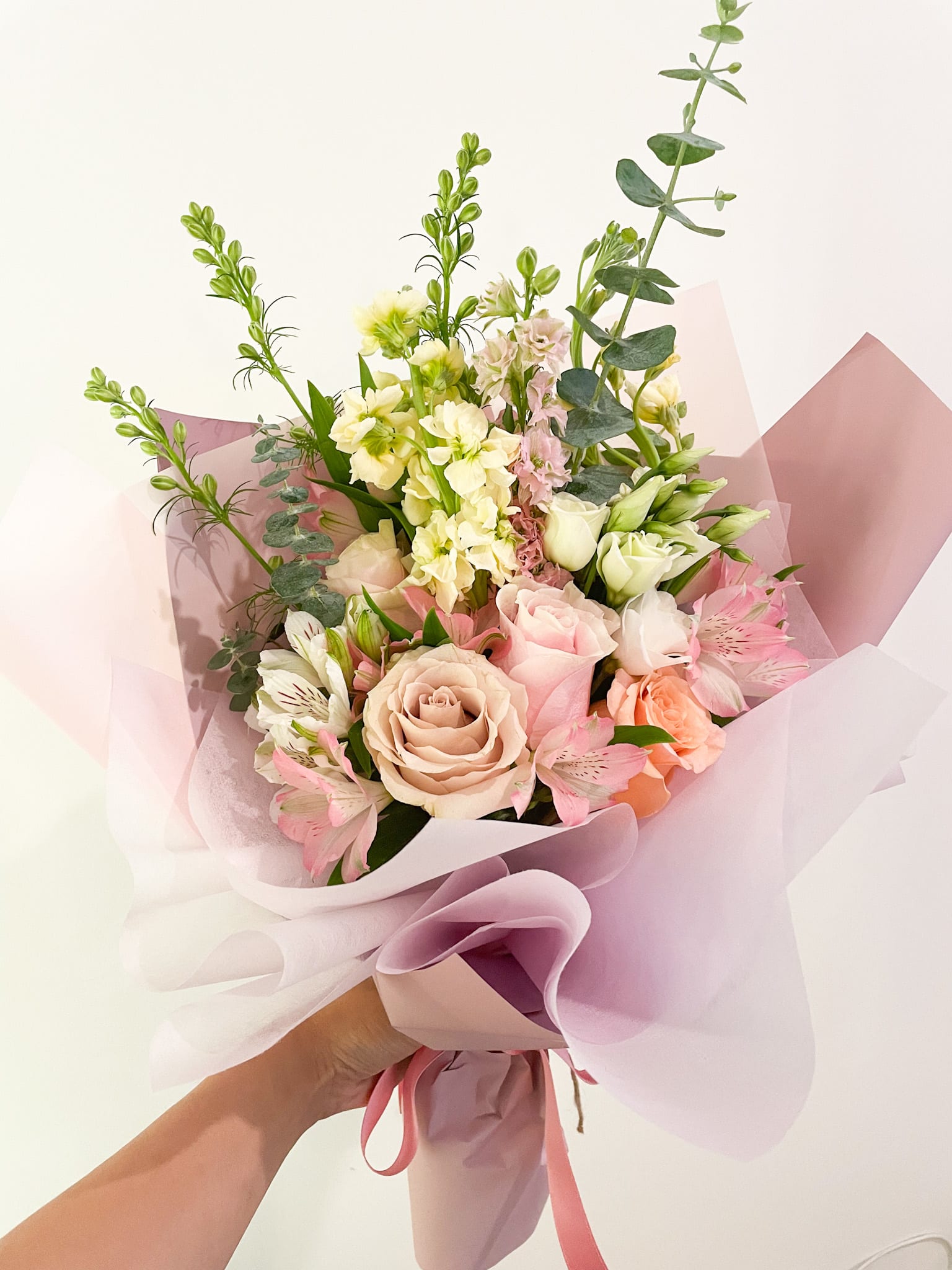 Handheld bouquet of pink and cream roses with pale filler flowers