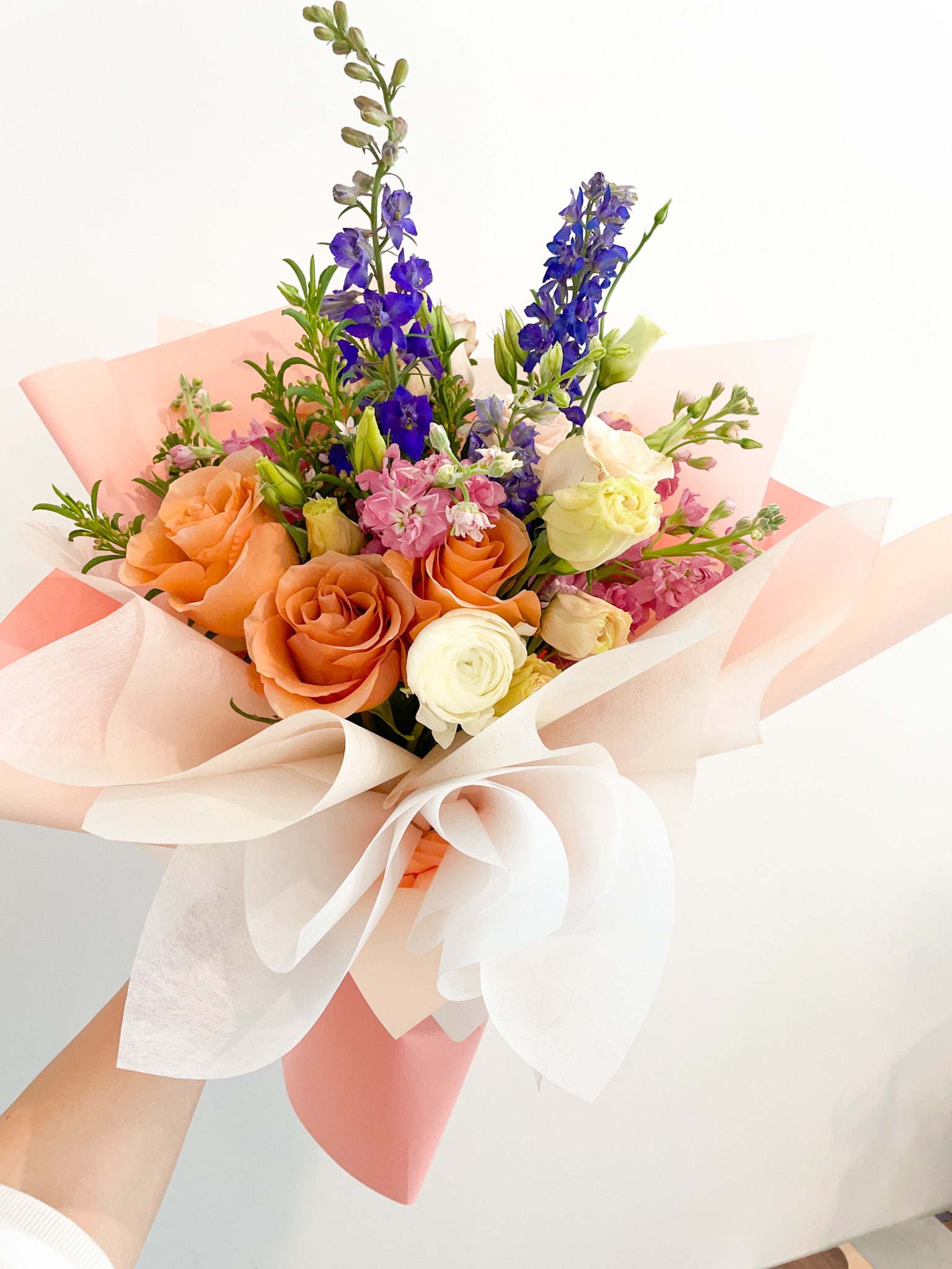 Hand-tied bouquet of orange, white, pink, and blue flowers in pastel wrapping