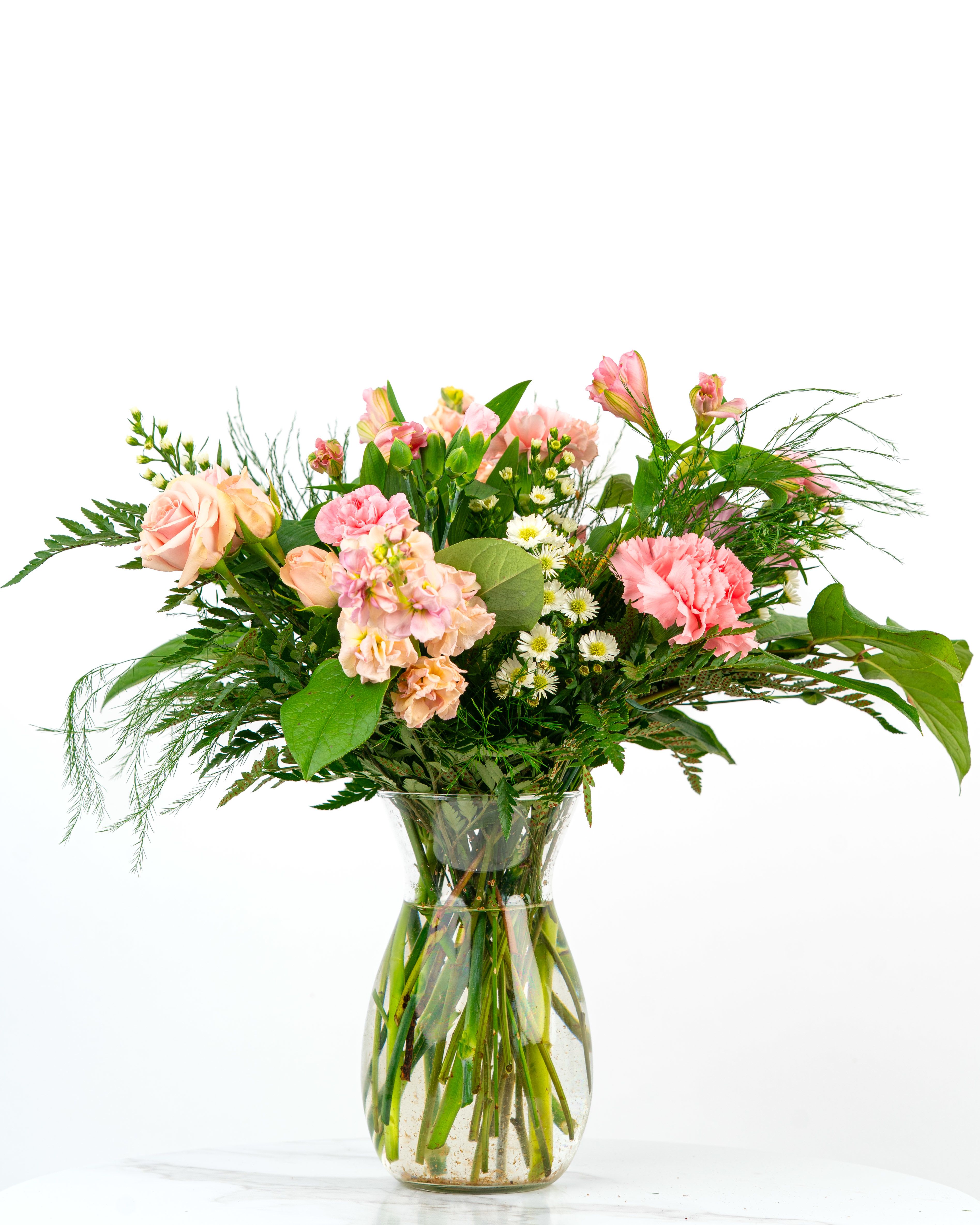 Pink and peach mixed flowers with white daisies arranged in a clear glass vase