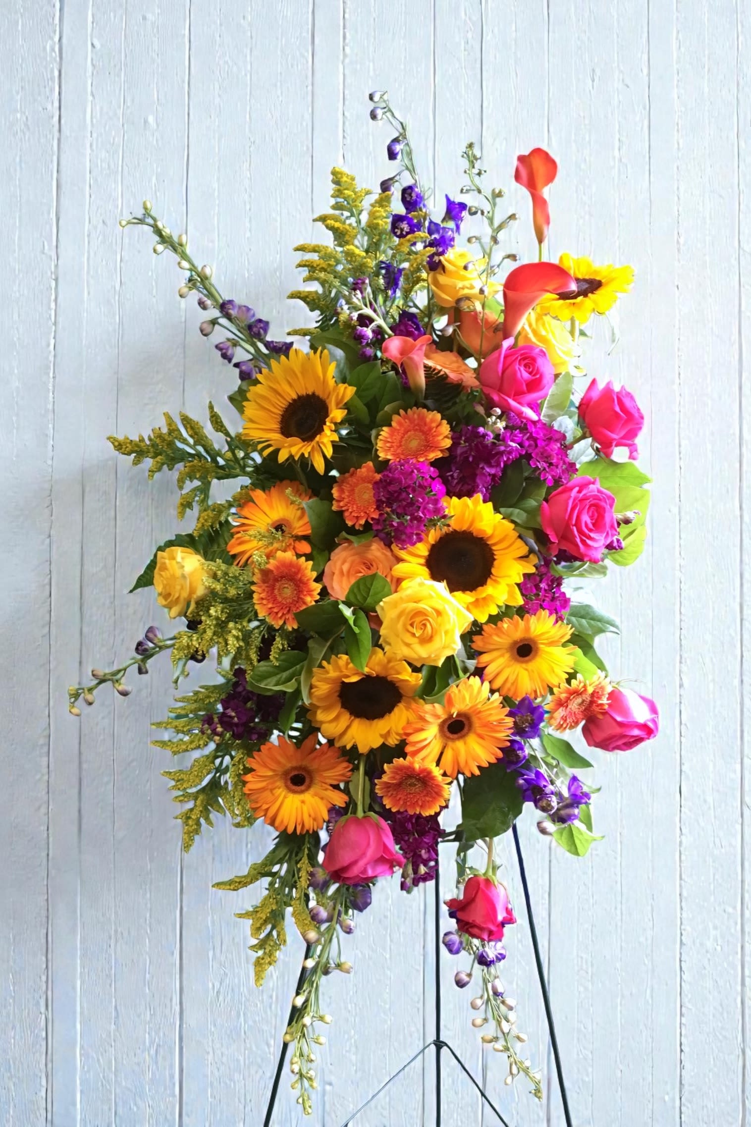 Harmony Easel Spray - Bright sunflowers, hot pink roses, orange gerbera and purple accents create a warm, garden-style easel spray suitable for sympathy and funeral tributes.