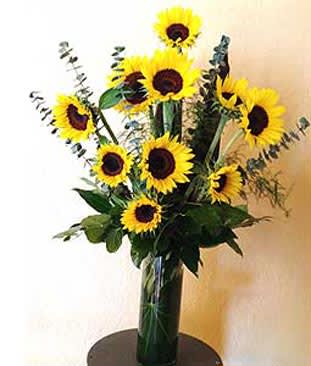 Tall arrangement of yellow sunflowers in a clear glass vase on a small round table
