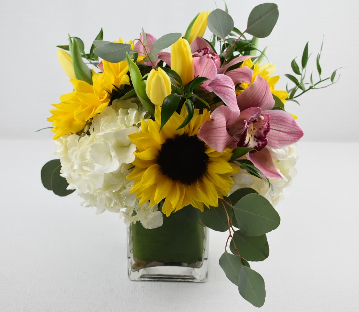 Bouquet of sunflowers, pink orchids, and white hydrangeas in a glass vase